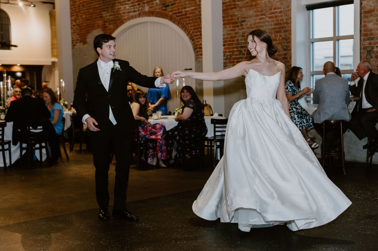 Bride and groom share first dance at wedding reception in rustic brick venue.