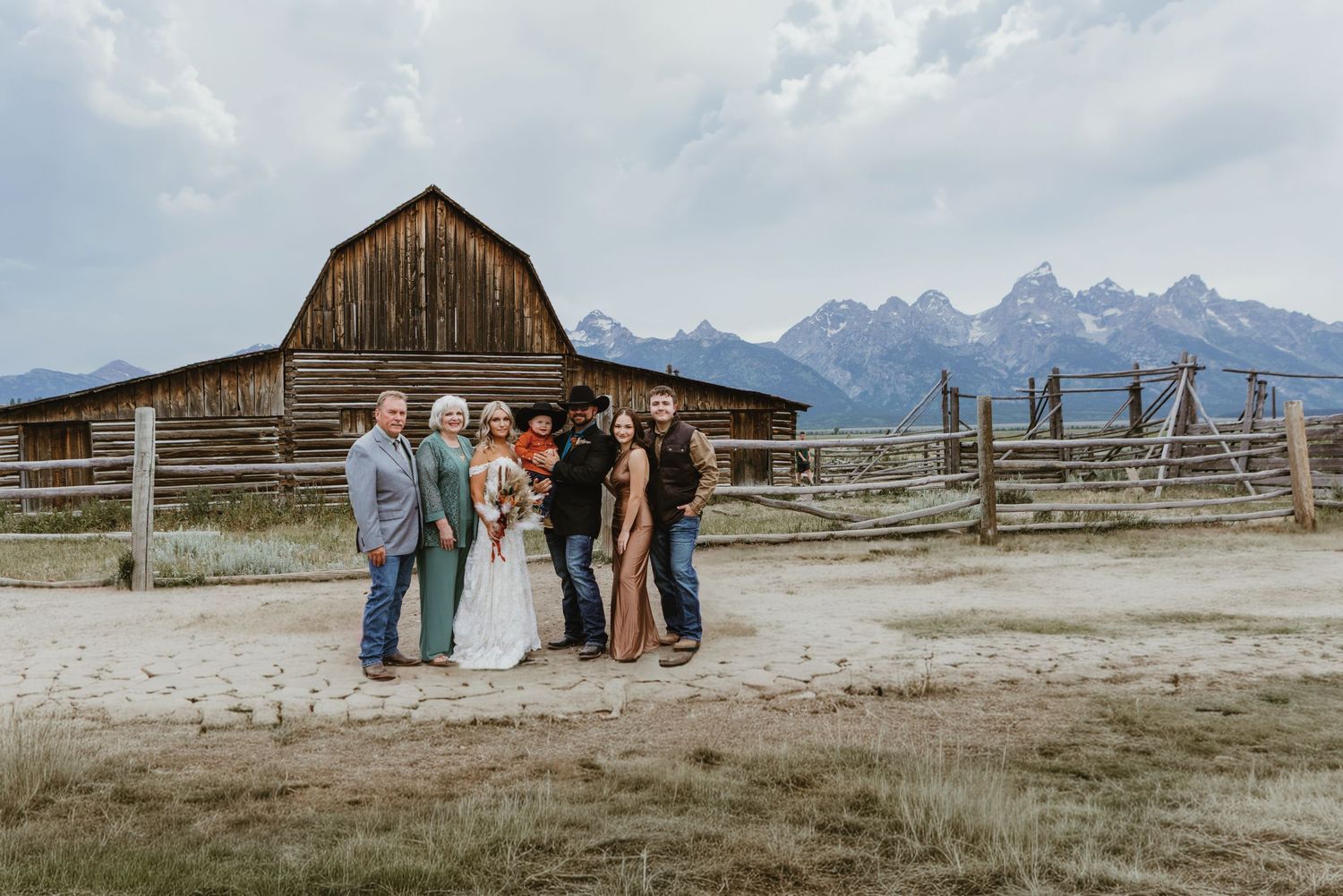 Wedding party poses before rustic barn with Grand Teton mountains backdrop in Jackson Hole Wyoming.