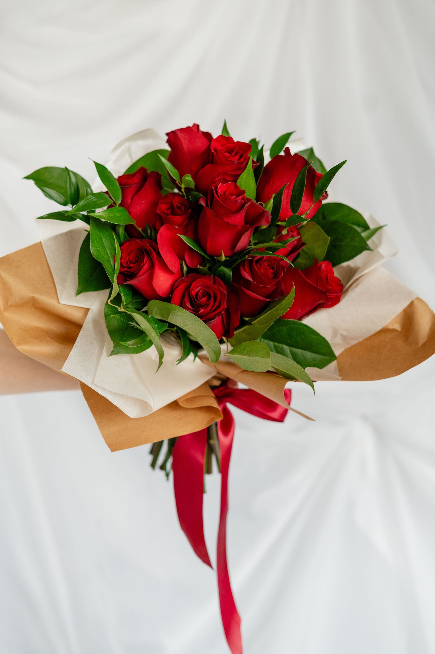 Beautiful red roses wrapped in brown kraft paper with a red ribbon accent against a white background.