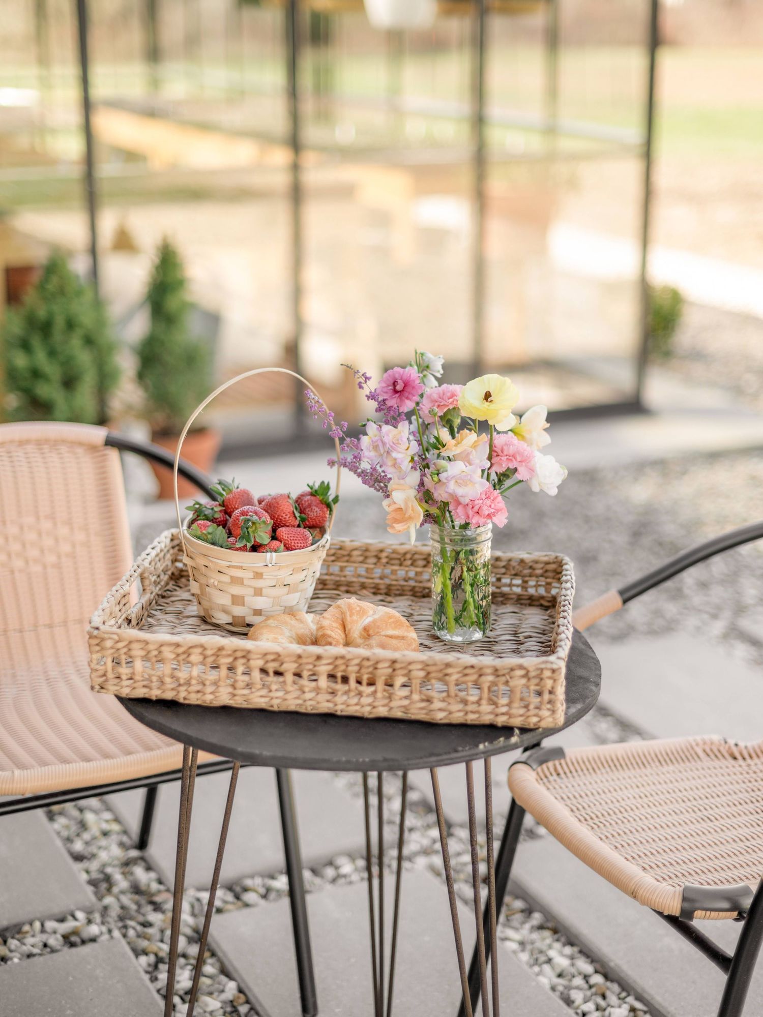 A rustic outdoor table setting with a woven tray holding fresh strawberries and pink flowers in a glass vase.