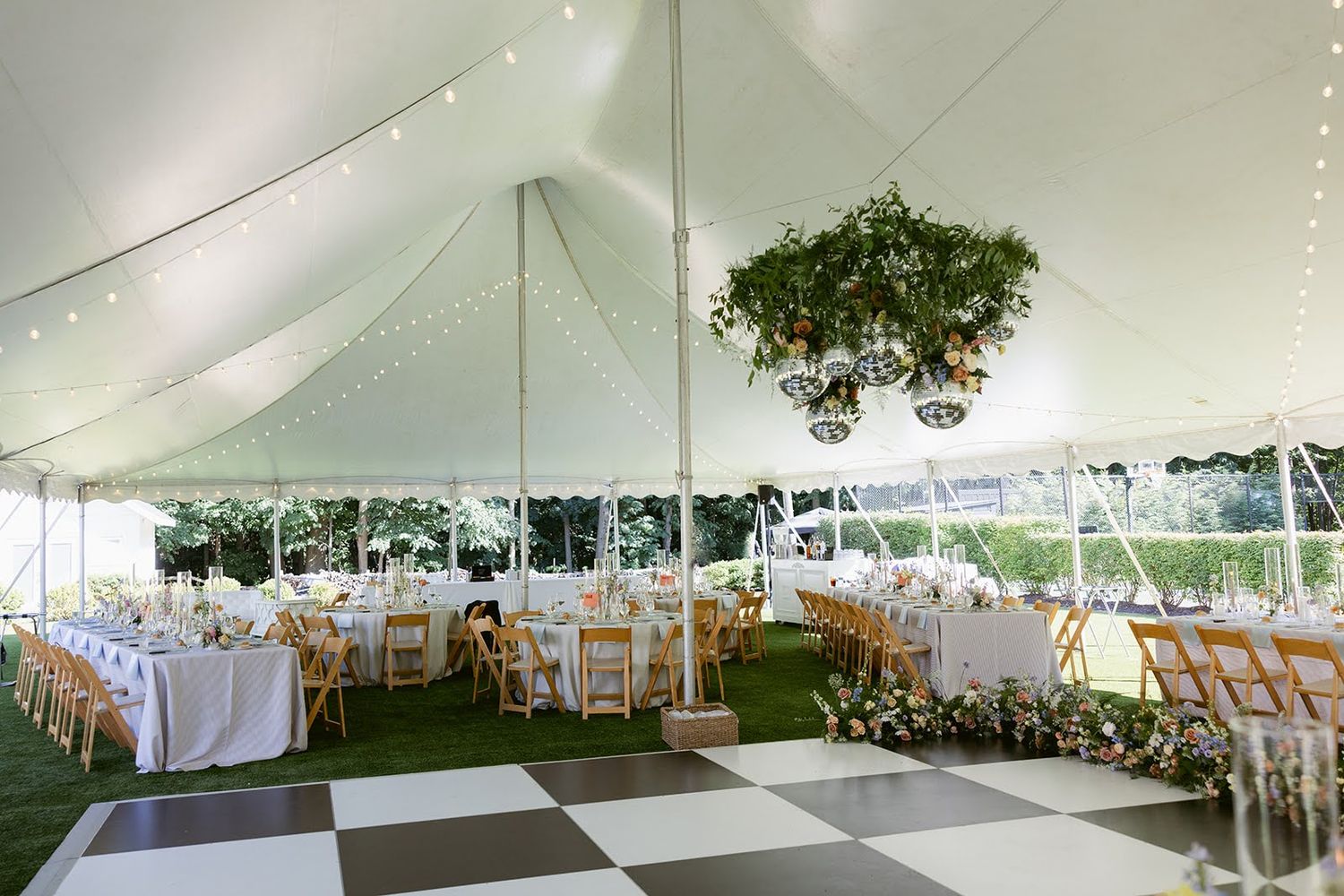 Elegant outdoor wedding reception tent with black and white dance floor, floral chandelier, and decorated dining tables.