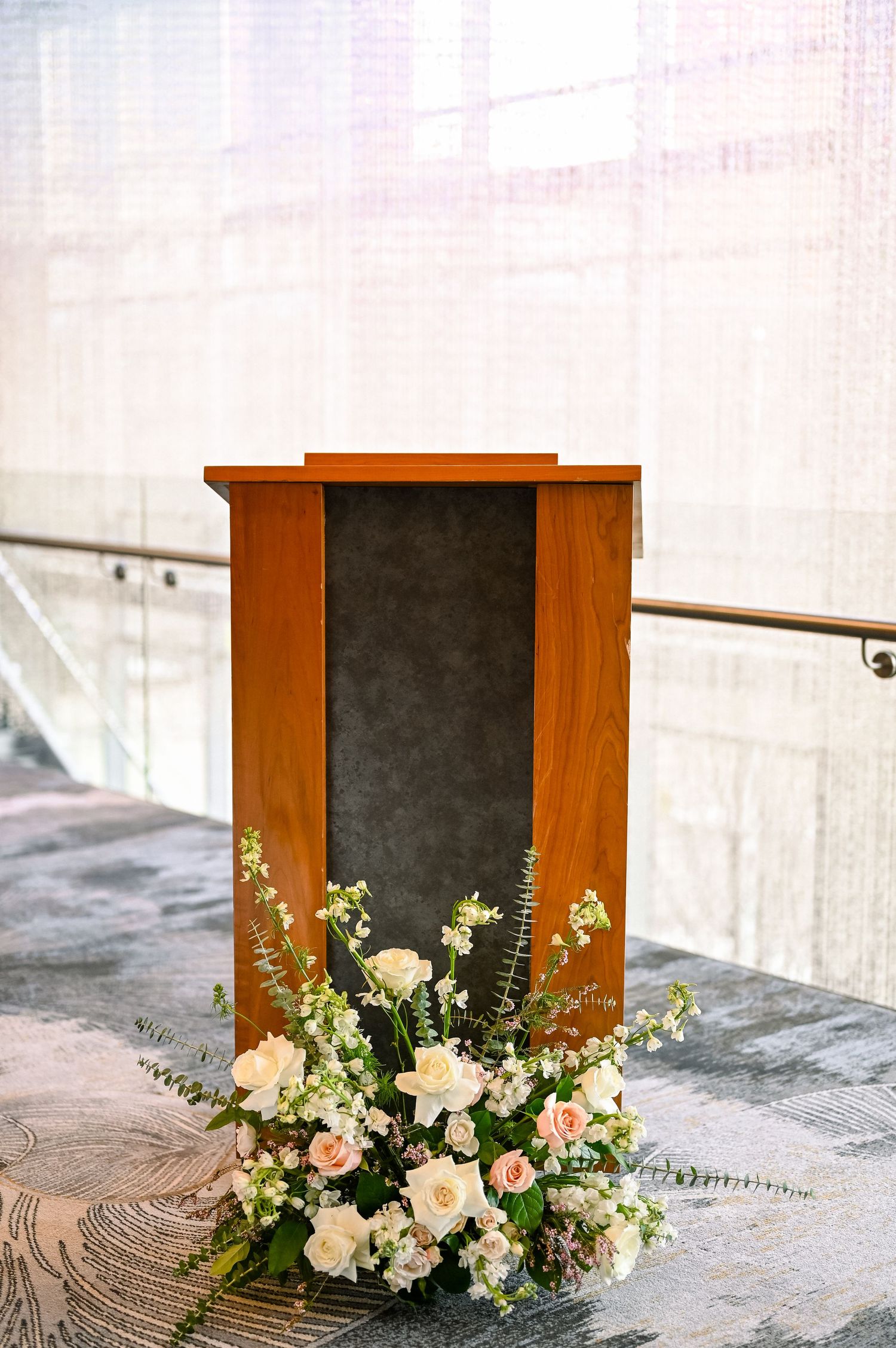 A wooden podium with blackboard front stands on concrete steps, decorated with an elegant white and pink floral arrangement.