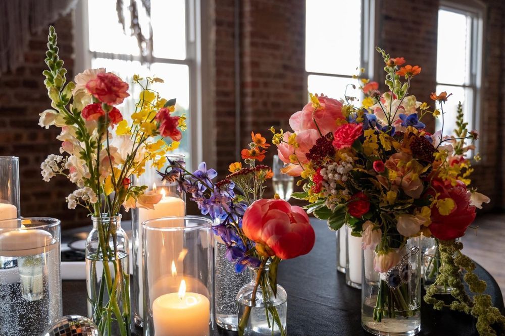 Colorful wildflower bouquets and glowing candles in glass vases decorate a rustic wedding reception table.