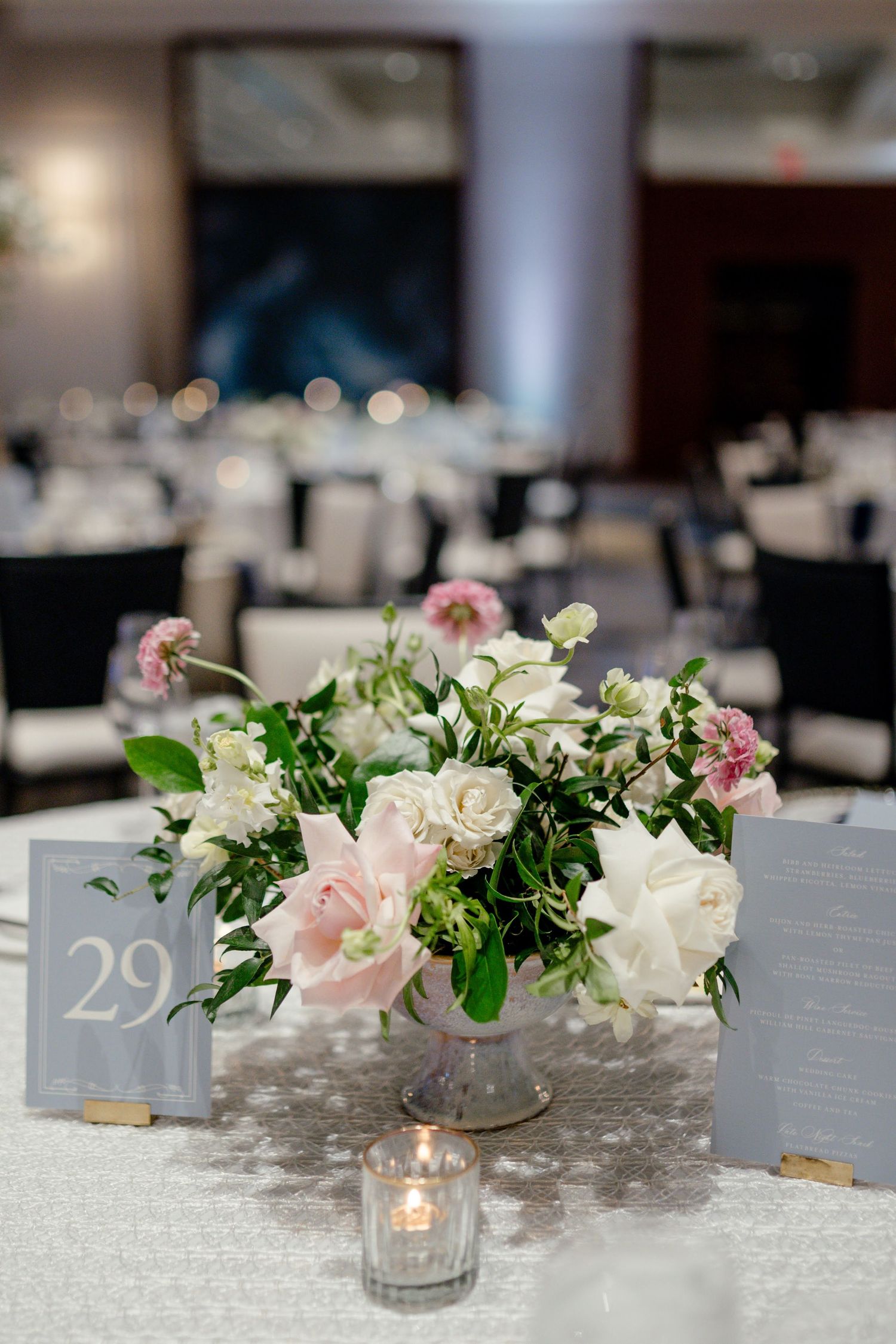 Elegant wedding reception centerpiece with pink and white flowers, greenery in glass vase, table number 29, candlelight.
