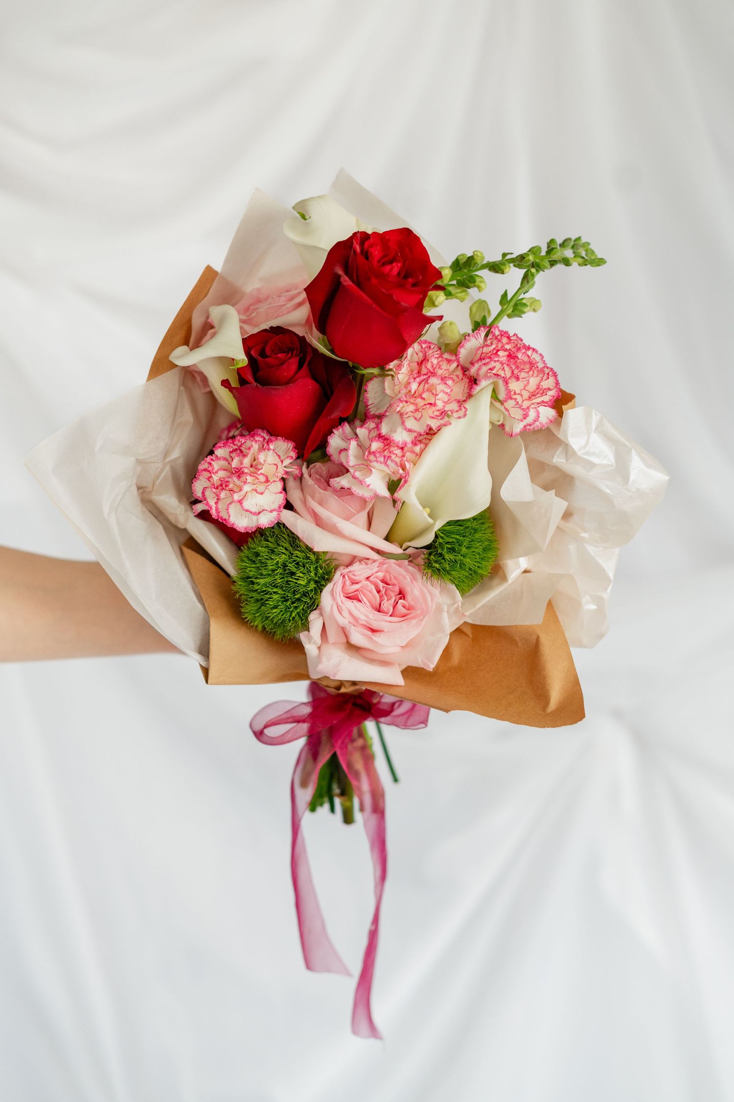 A romantic bouquet wrapped in brown paper features pink and red roses with green accents and a burgundy ribbon.