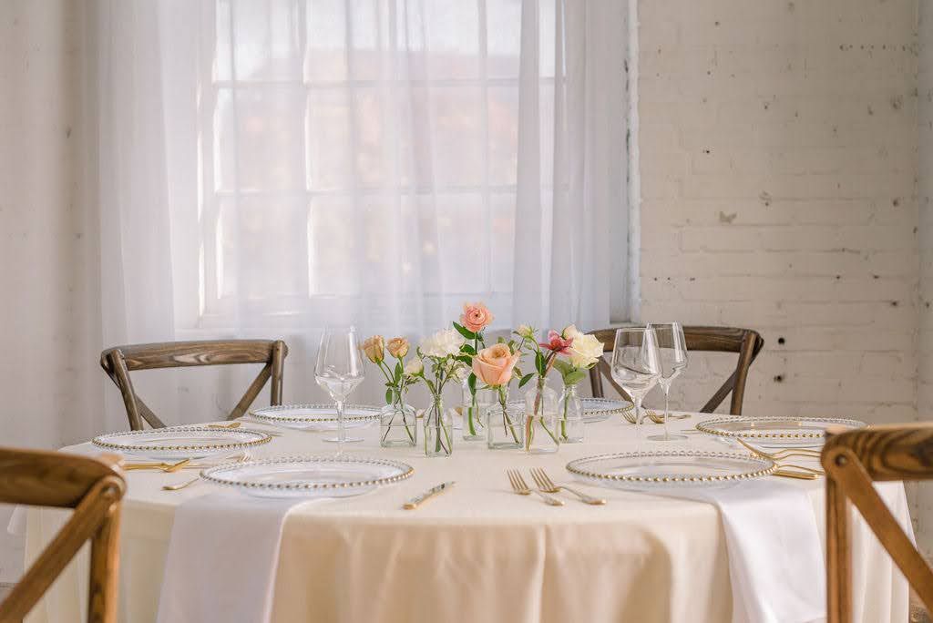 Elegant wedding table setting with peach roses, crystal glasses, and gold cutlery on white linen.