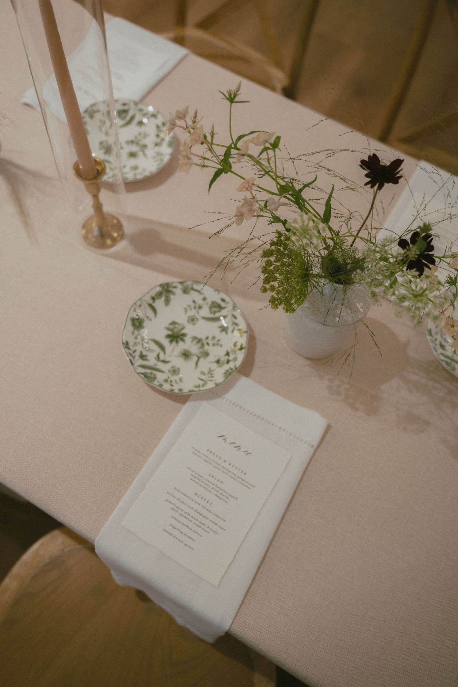 Elegant wedding table setting with floral plates, taper candles, wildflower centerpiece, and a printed menu on white linen.