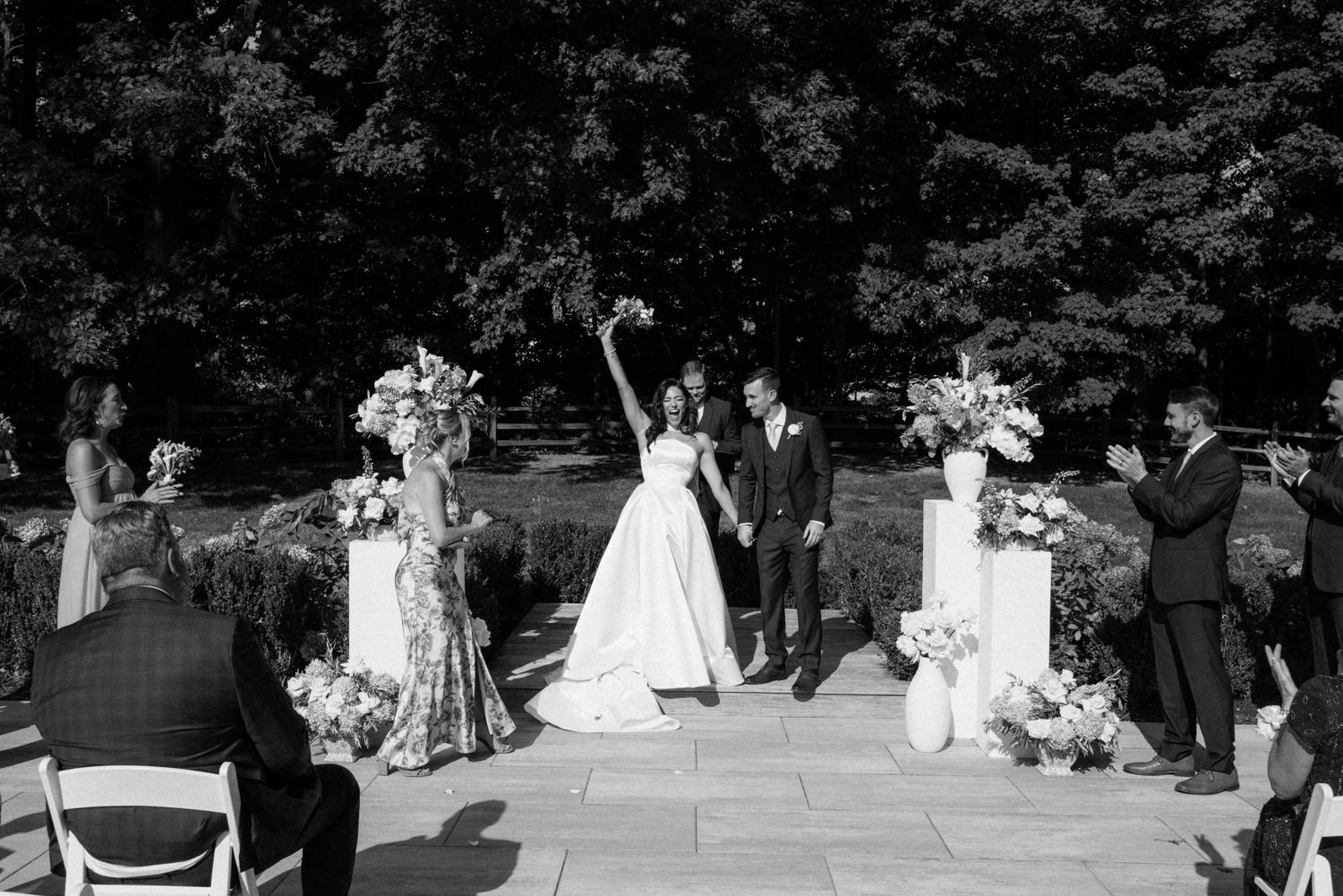A wedding party poses together in a formal garden setting during an outdoor celebration.