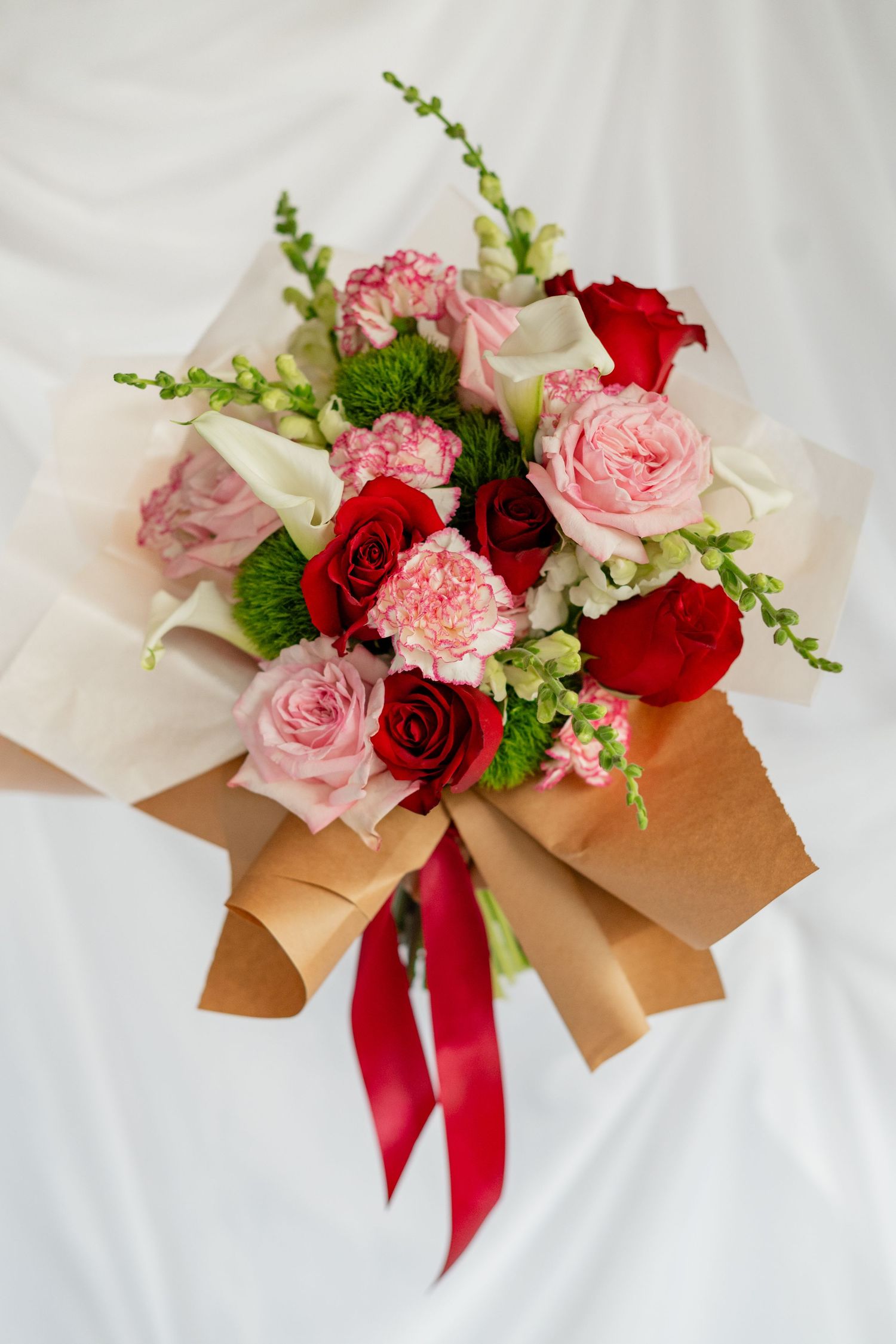 A sequence of floral arrangements with pink and red roses wrapped in kraft paper with red ribbon accents on white fabric.