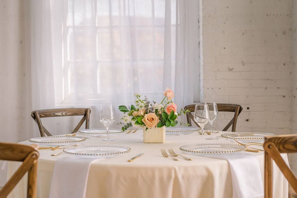 Elegant wedding table setting with peach floral centerpiece, crystal glasses, and gold cutlery on white linen.