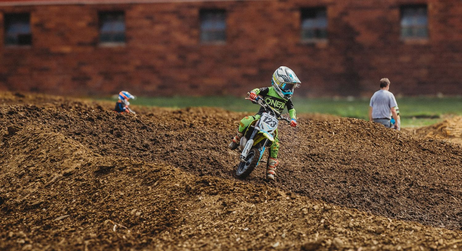 Motocross rider launches off a dirt jump during a 74 Promotions racing event, kicking up dust and catching major air