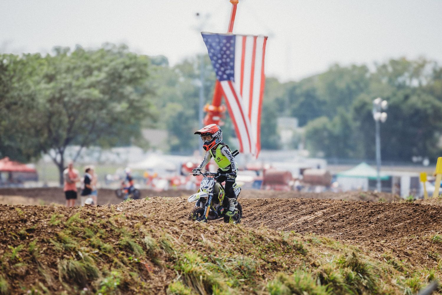 Motocross rider launches off a dirt jump during a 74 Promotions racing event, kicking up dust and catching major air