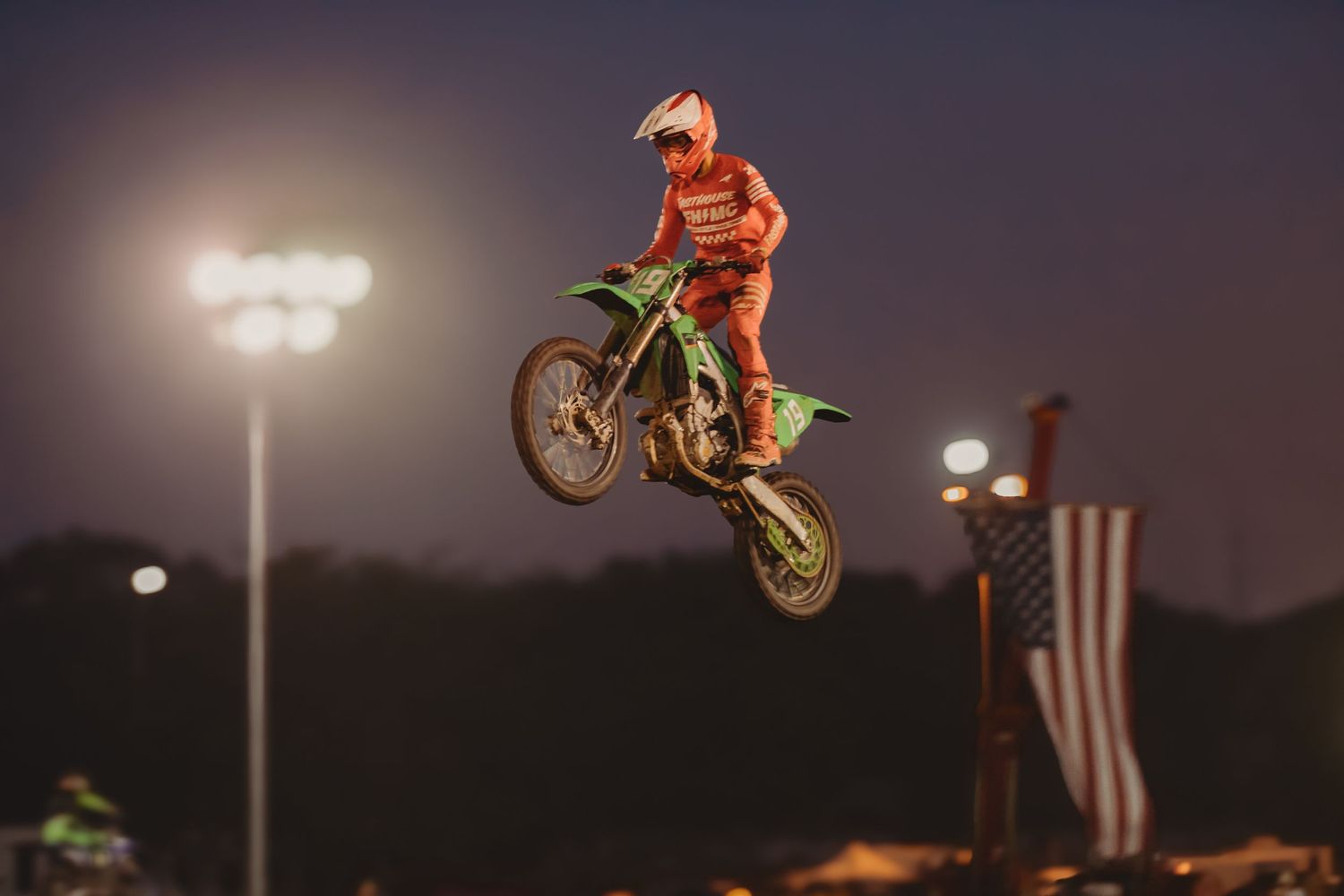 Motocross rider launches off a dirt jump during a 74 Promotions racing event, kicking up dust and catching major air