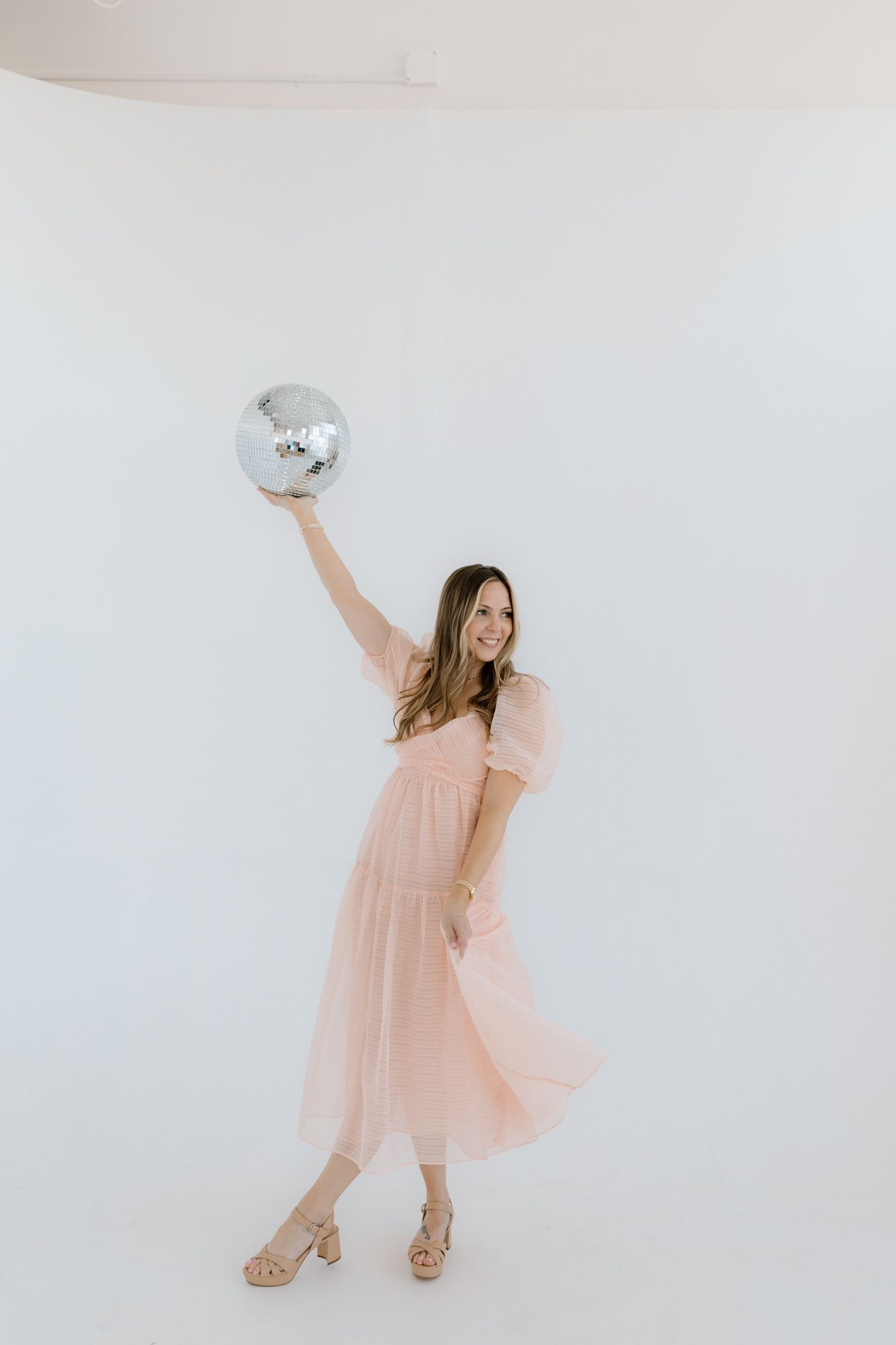 Person in flowing pink dress dancing with disco ball in white studio setting Chattanooga Branding