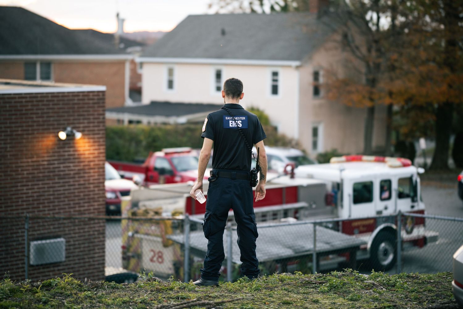 A firefighter in navy blue uniform stands overlooking a fire truck parked below on a residential street.