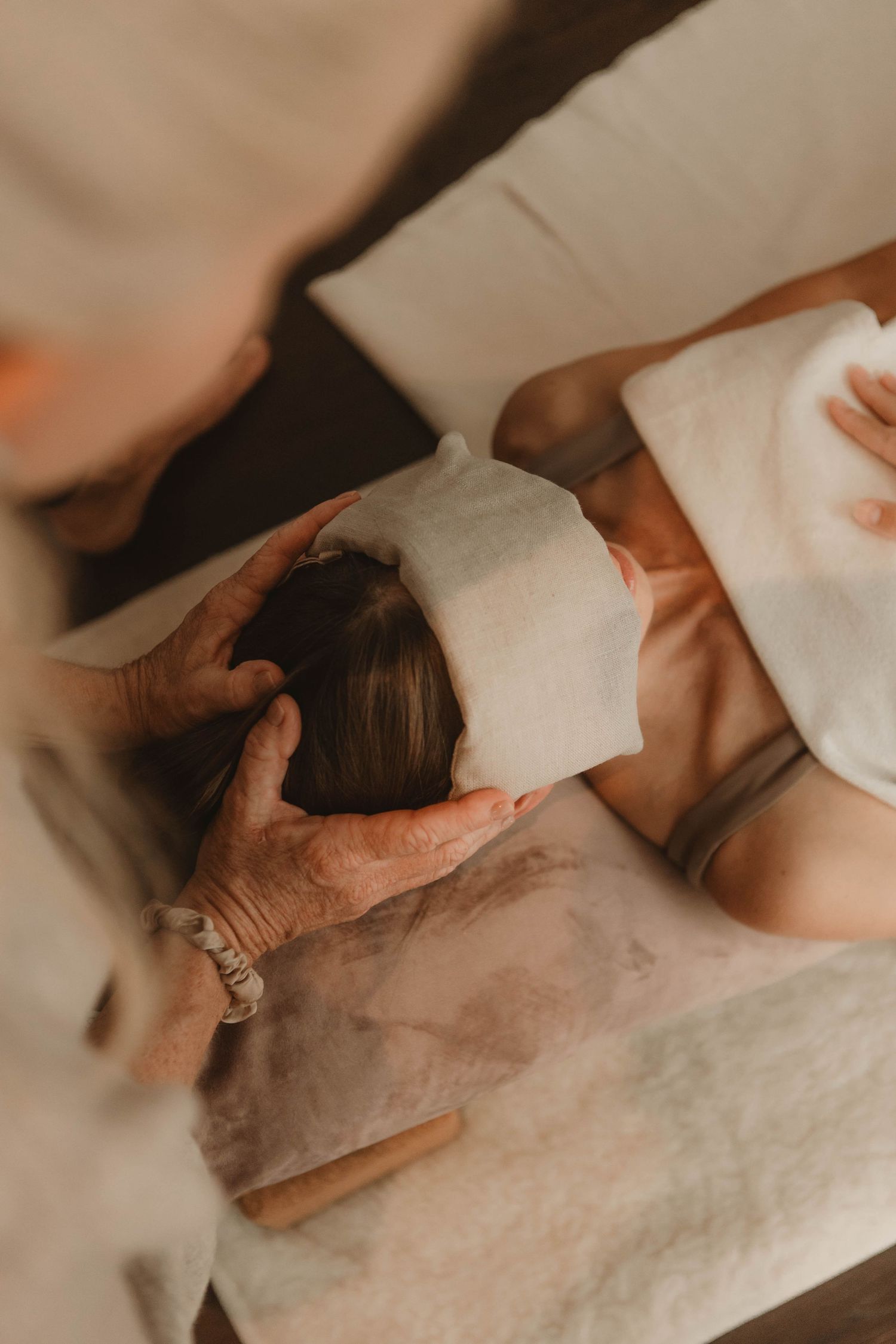 Person receiving a relaxing facial massage with white towels on a spa treatment table in warm lighting.