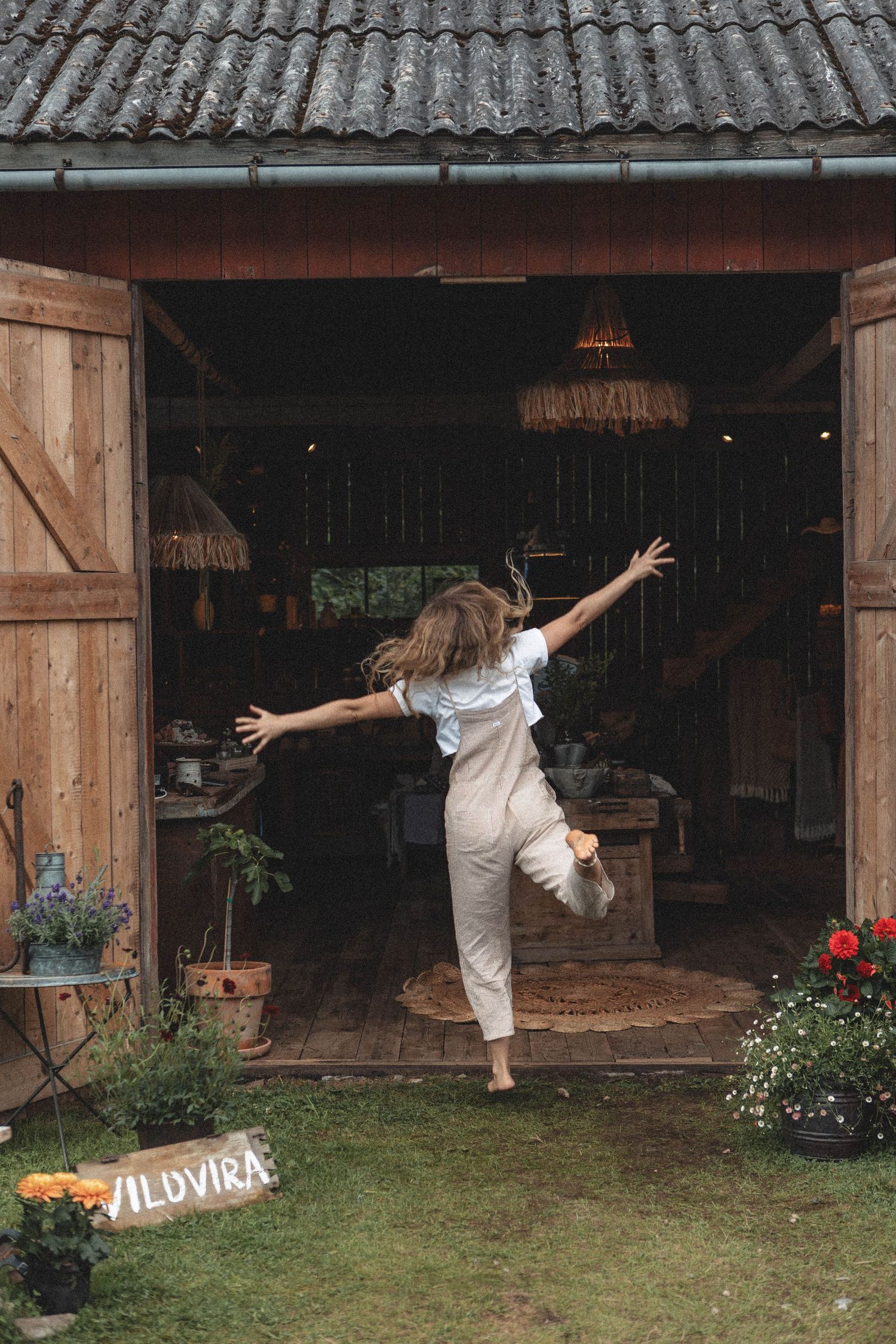 Dancing figure in overalls at rustic barn entrance with flowers and thatched roof.