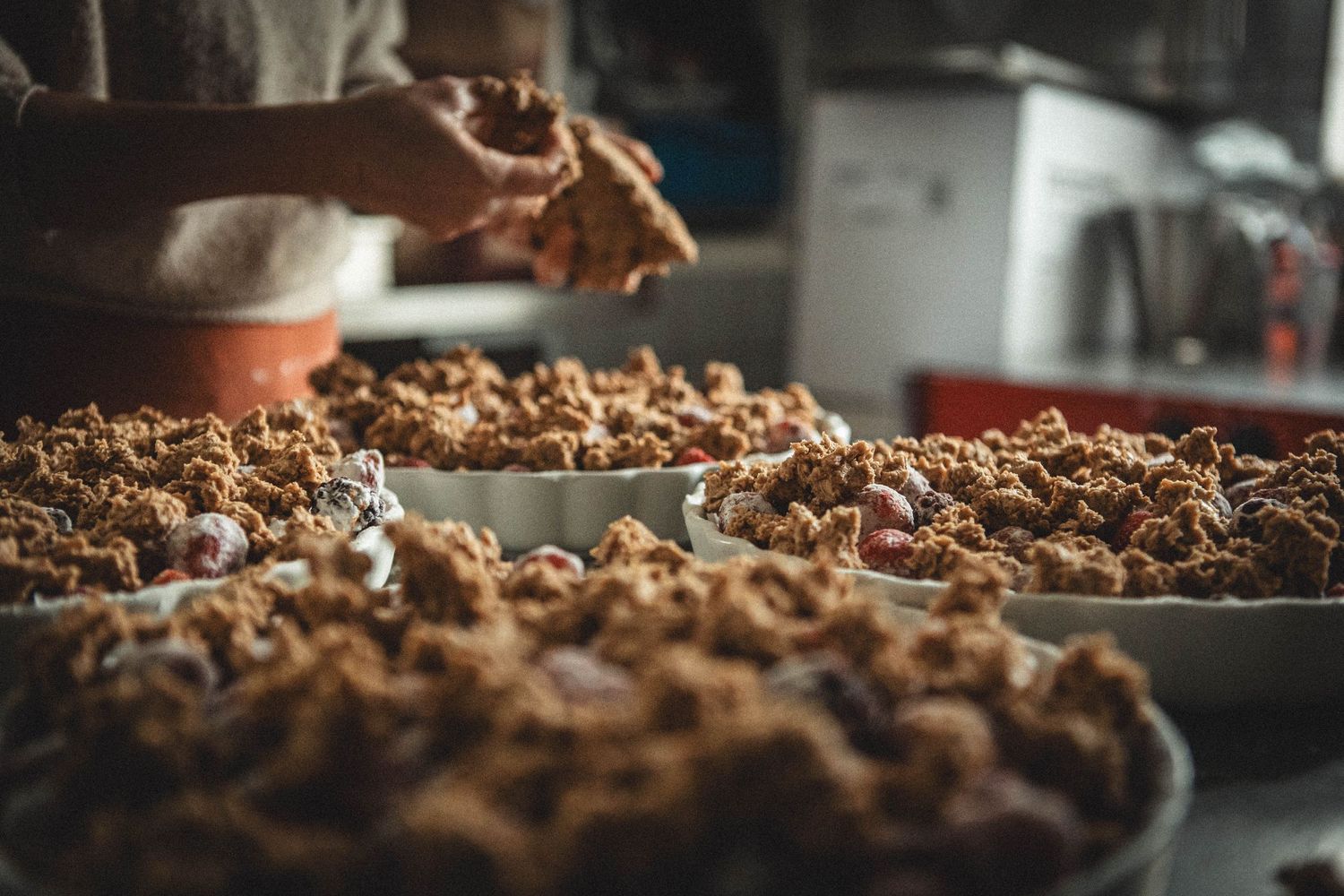 Hands working with a large batch of crumbly baked mixture in a commercial kitchen.