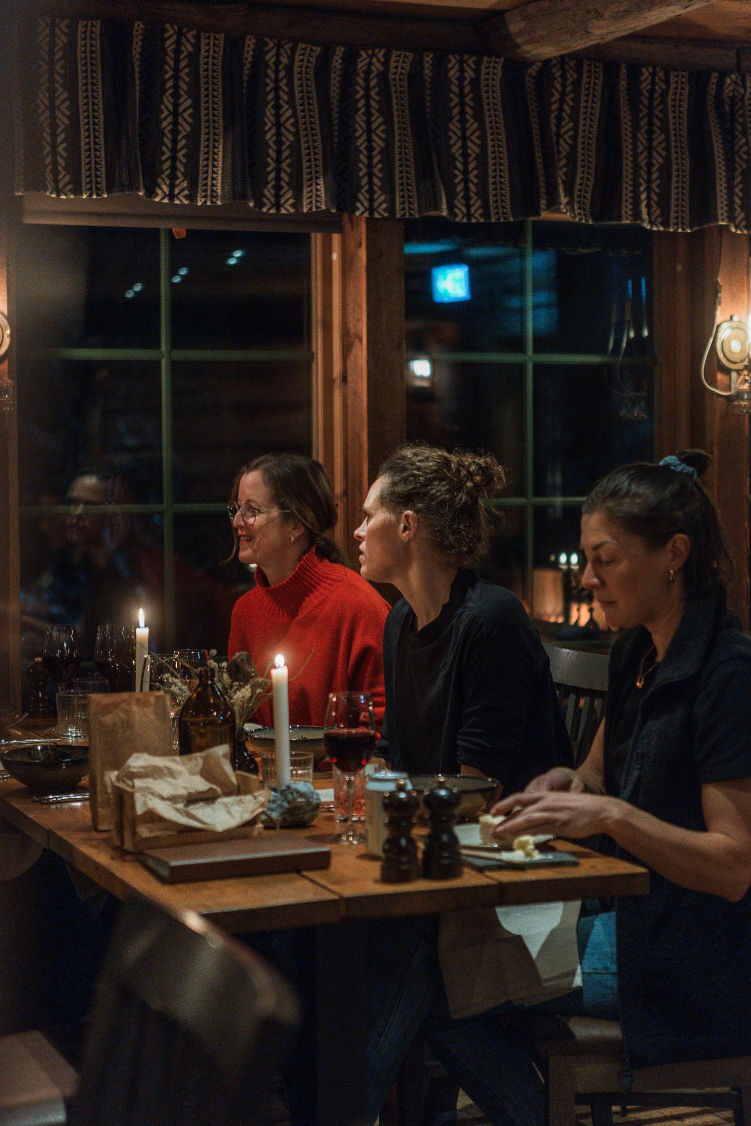 Guests dining by candlelight at a rustic wooden table in a cozy cabin setting.