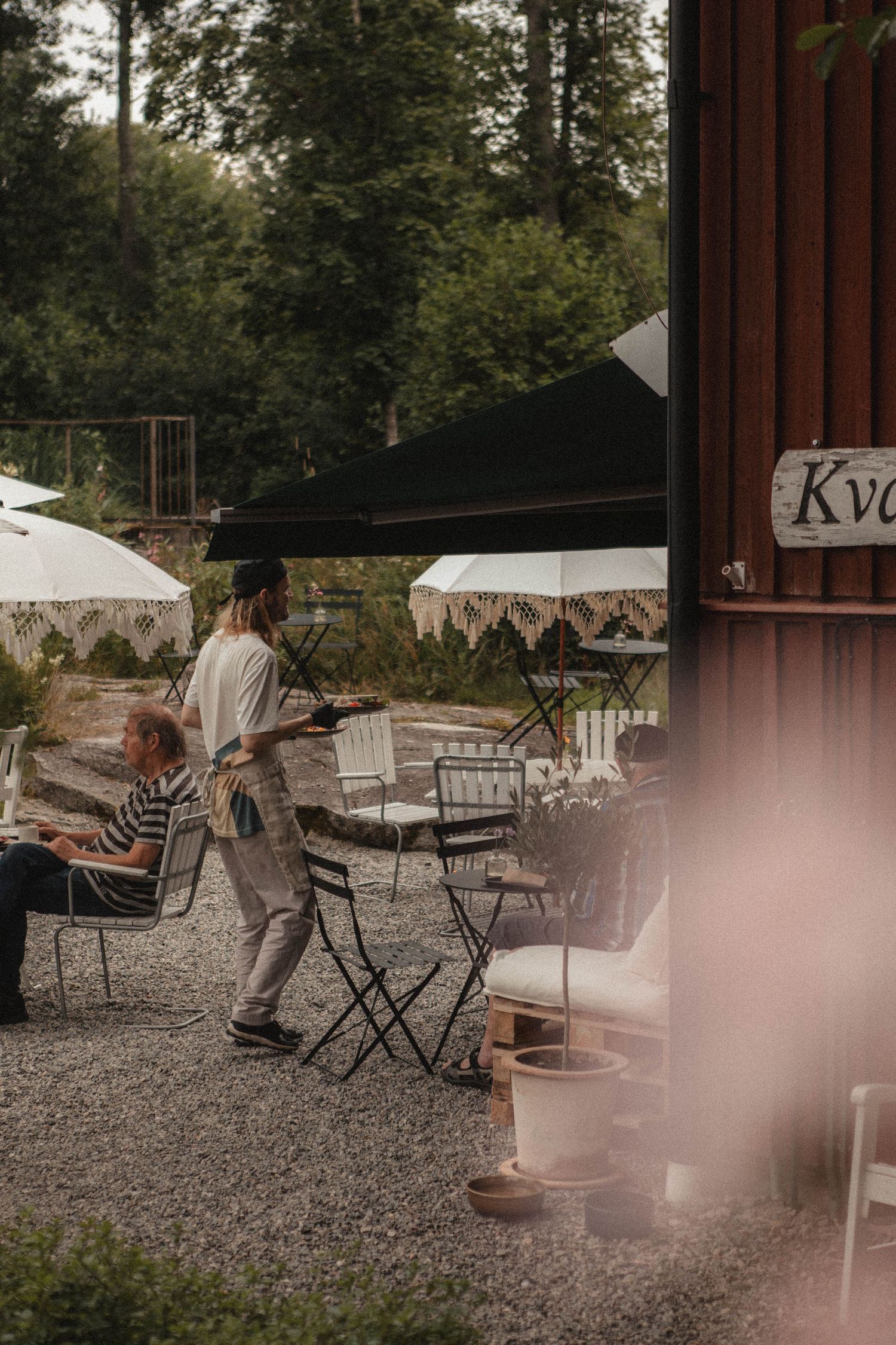 Outdoor cafe seating area with white umbrellas and gravel ground near a red building.