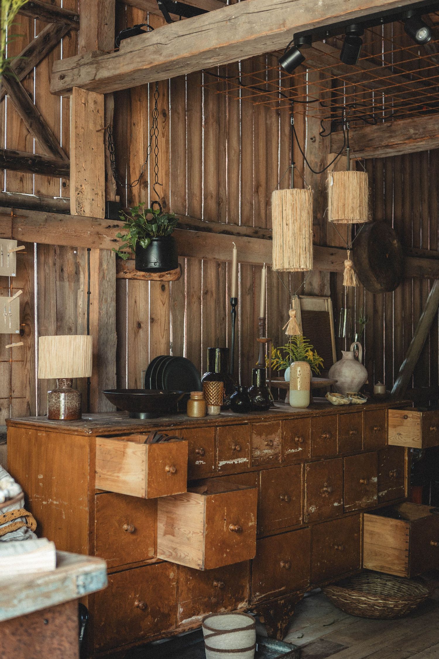 Rustic wooden storage system with multiple drawers and hanging pendant lights in barn-like setting.