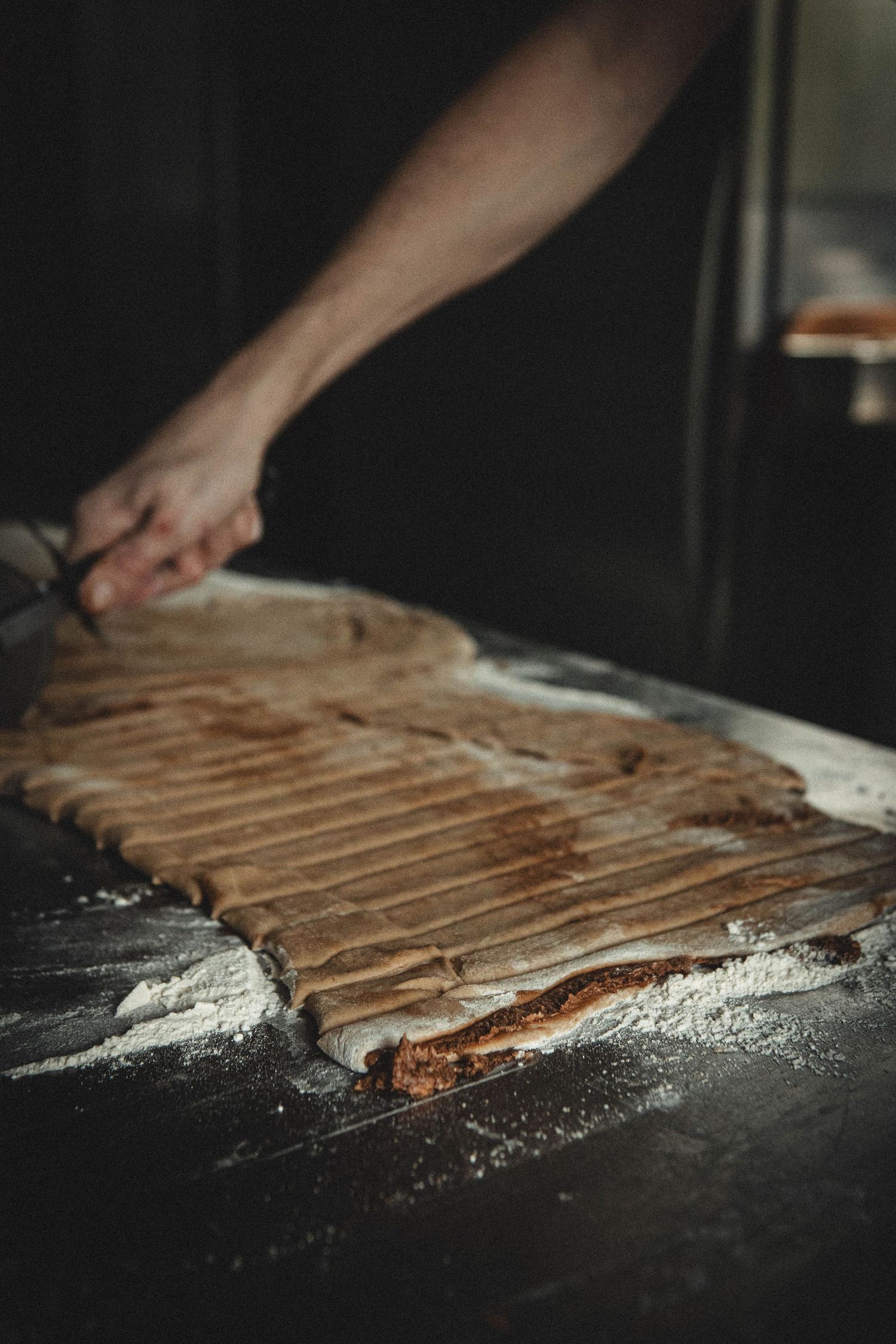 Baker scoring lines into raw bread dough on a floured surface.