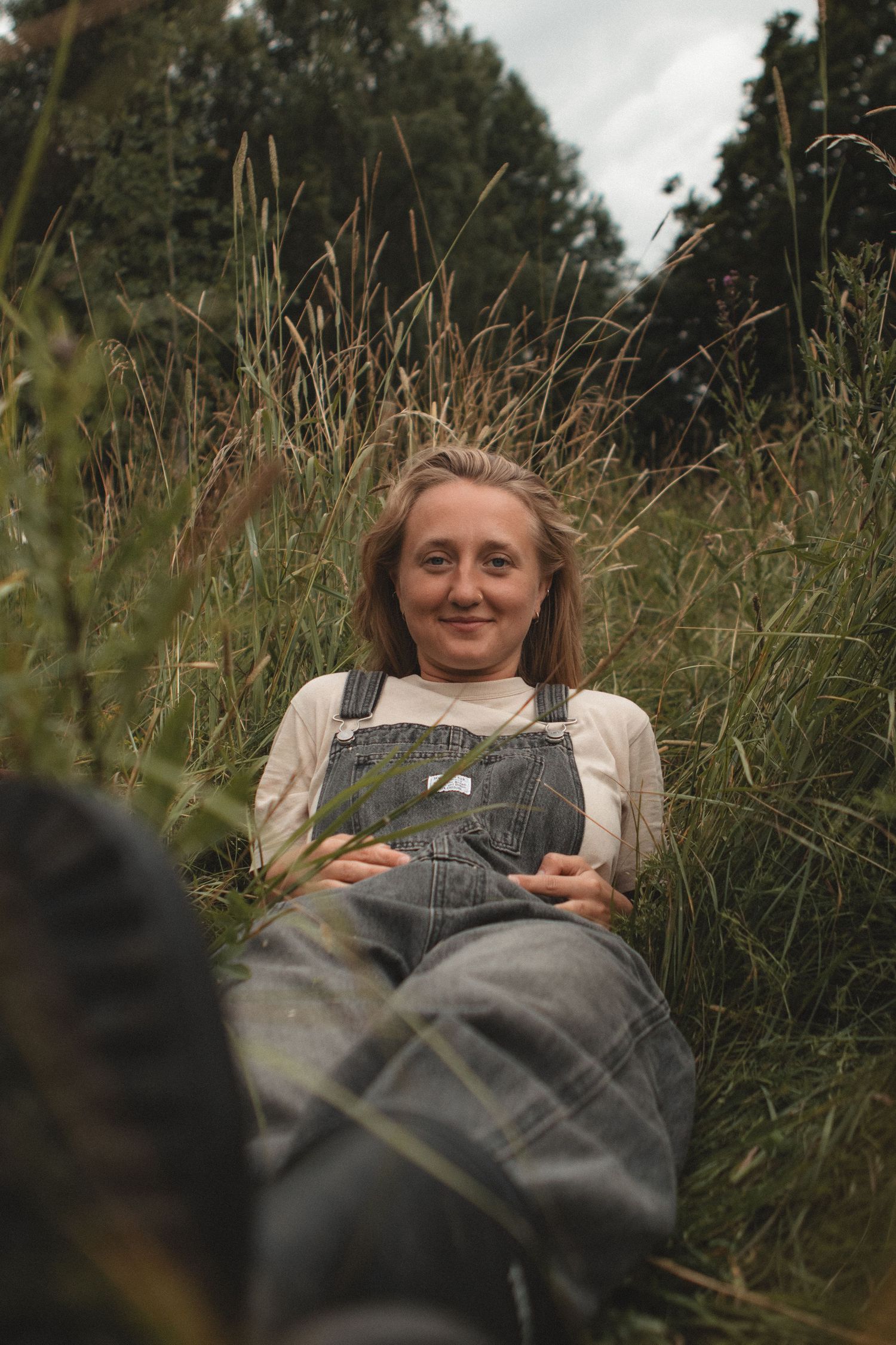 Person in overalls lies contentedly among tall wild grasses on a summer day.