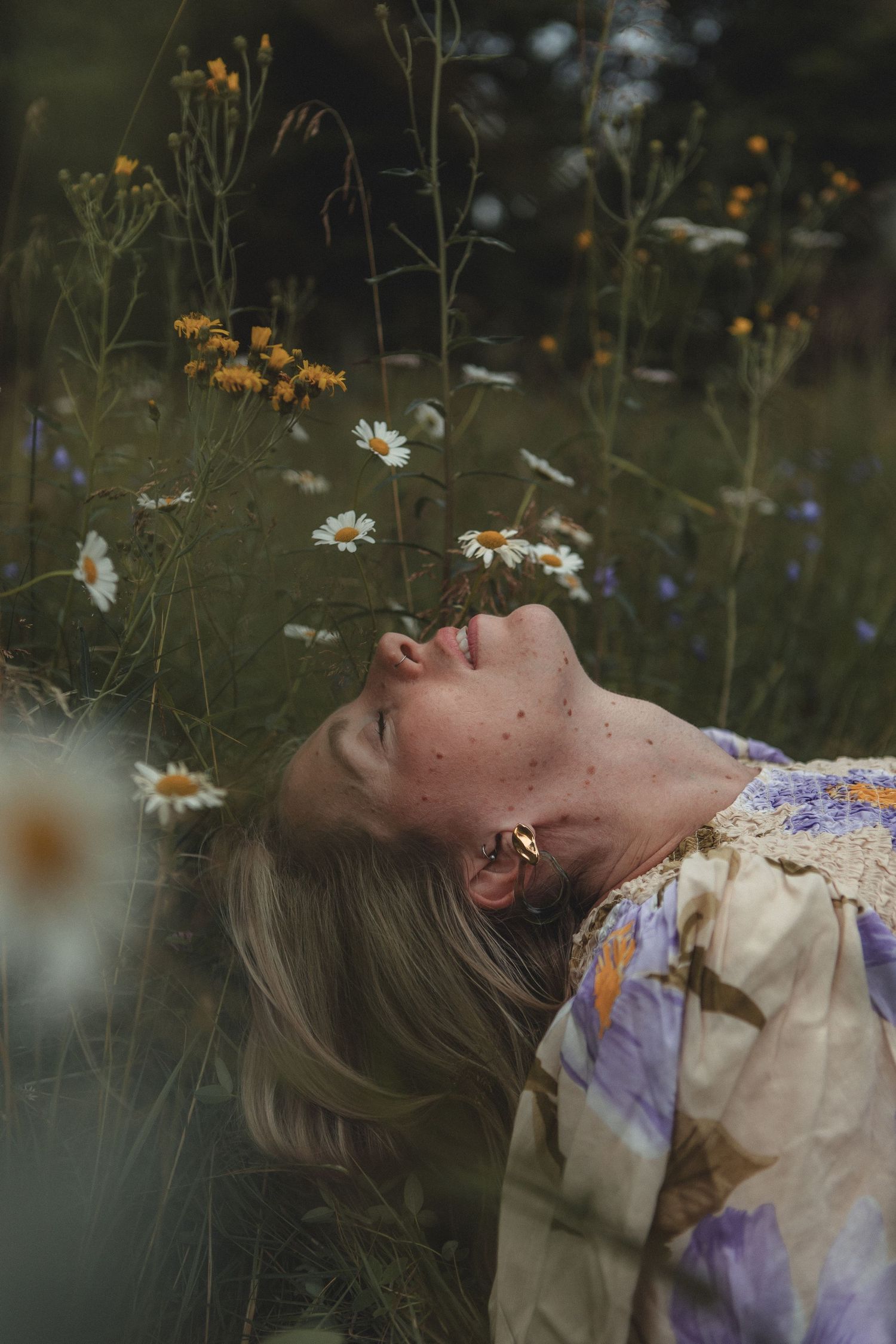 Ethereal portrait in a wildflower meadow with daisies and yellow flowers against a moody dark background.