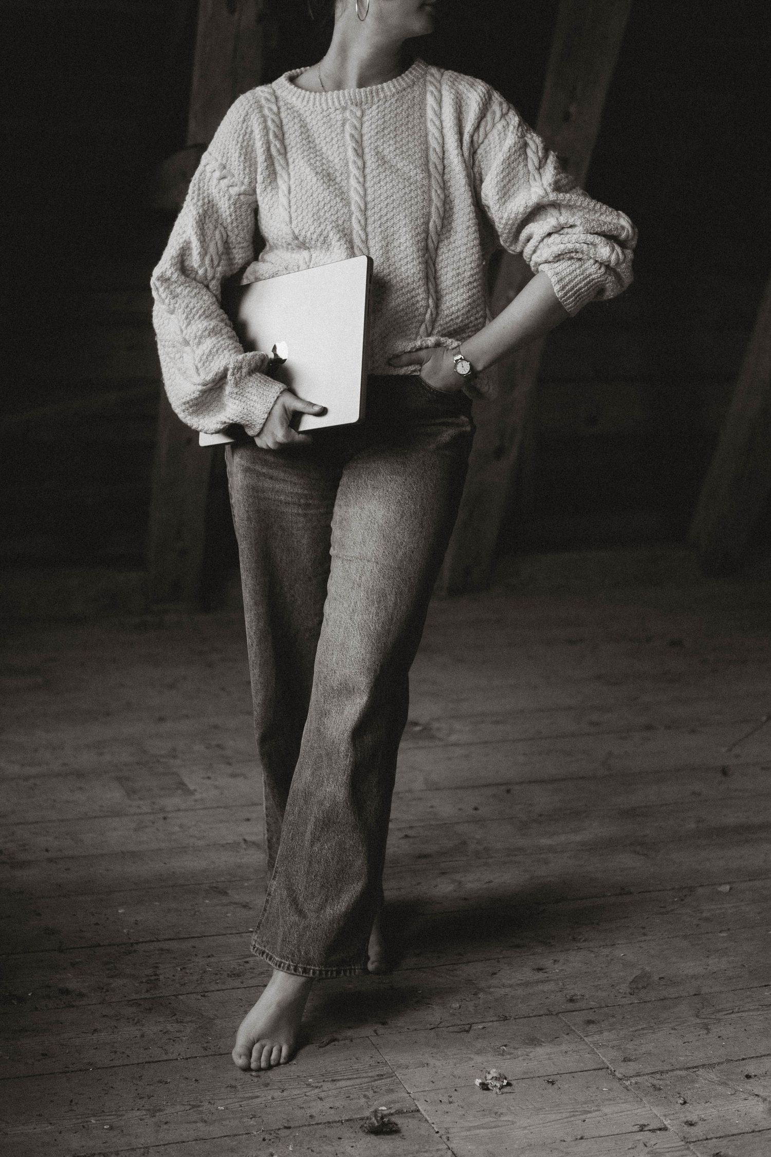 Person in white sweater and jeans sitting barefoot on rustic wooden floor.