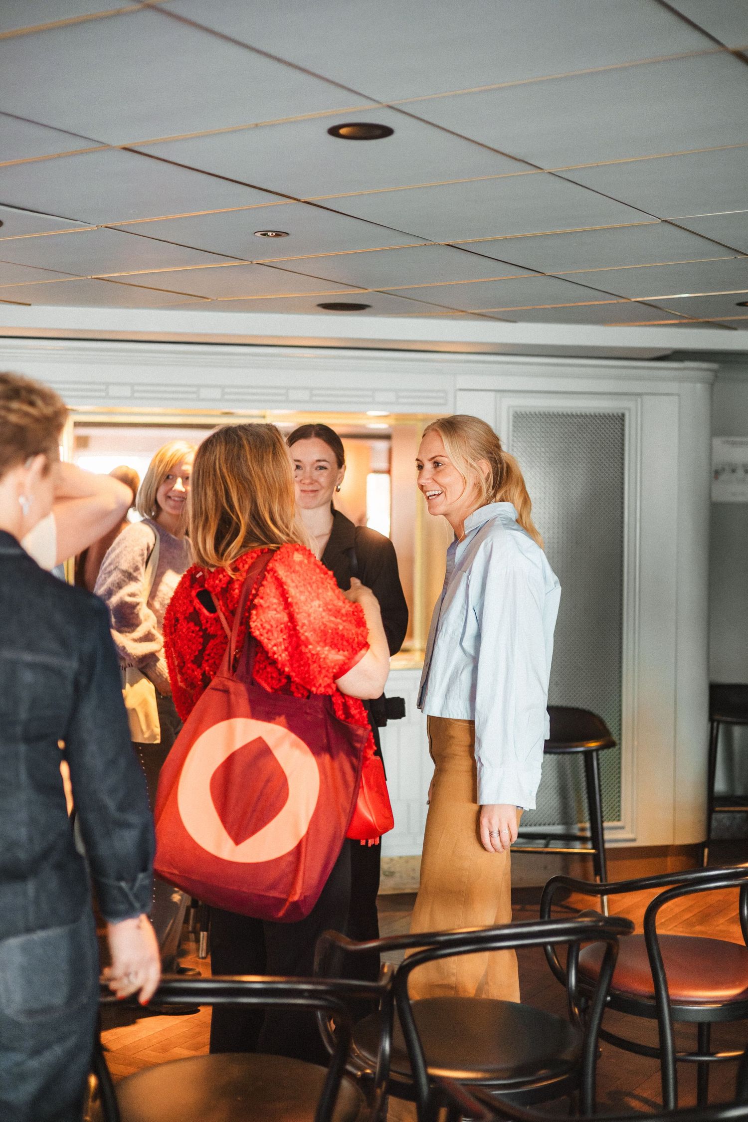 People interacting in a room with chairs and drop ceiling tiles.