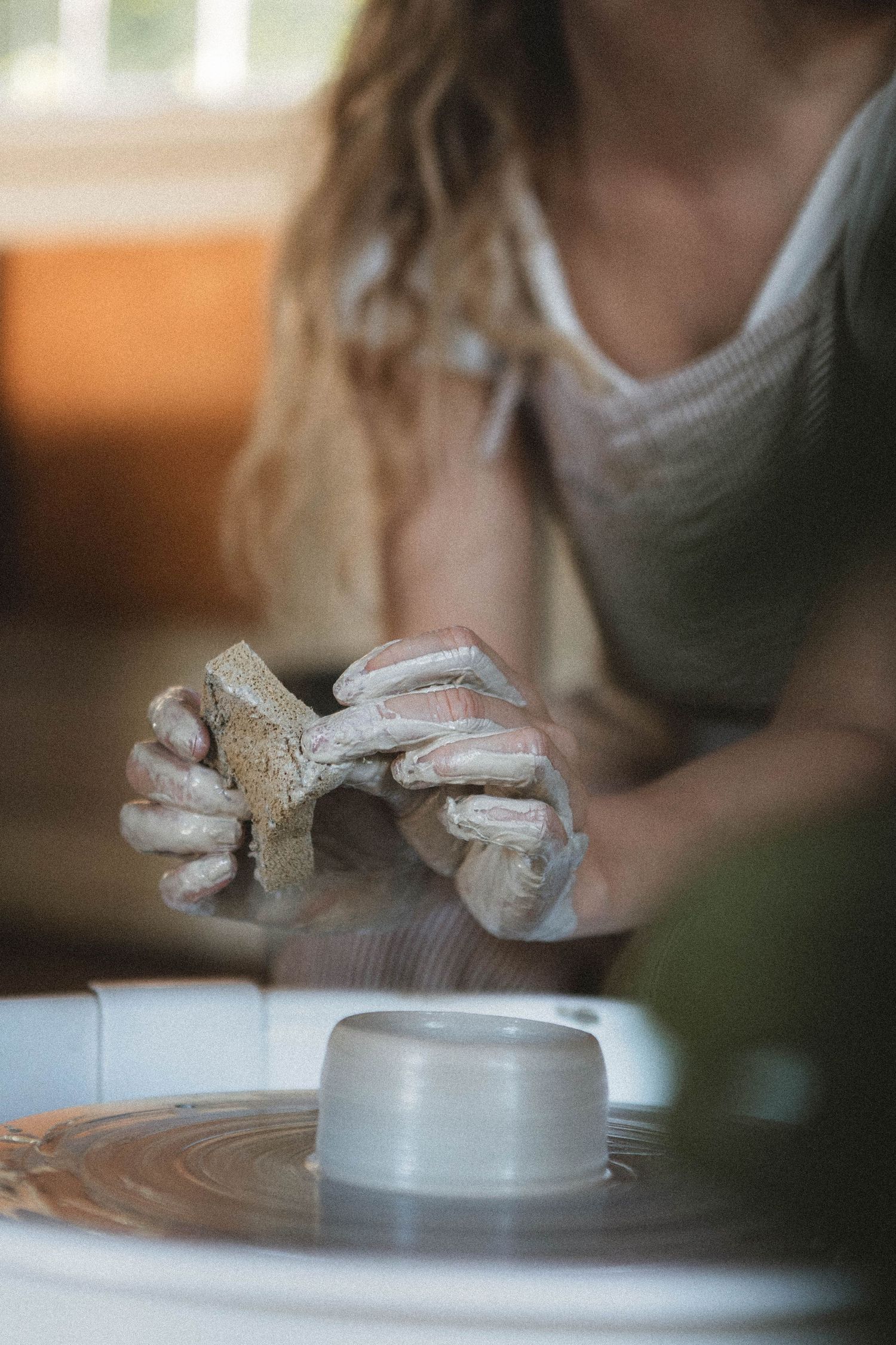 Close-up of hands carefully shaping a small clay vessel on a pottery wheel.