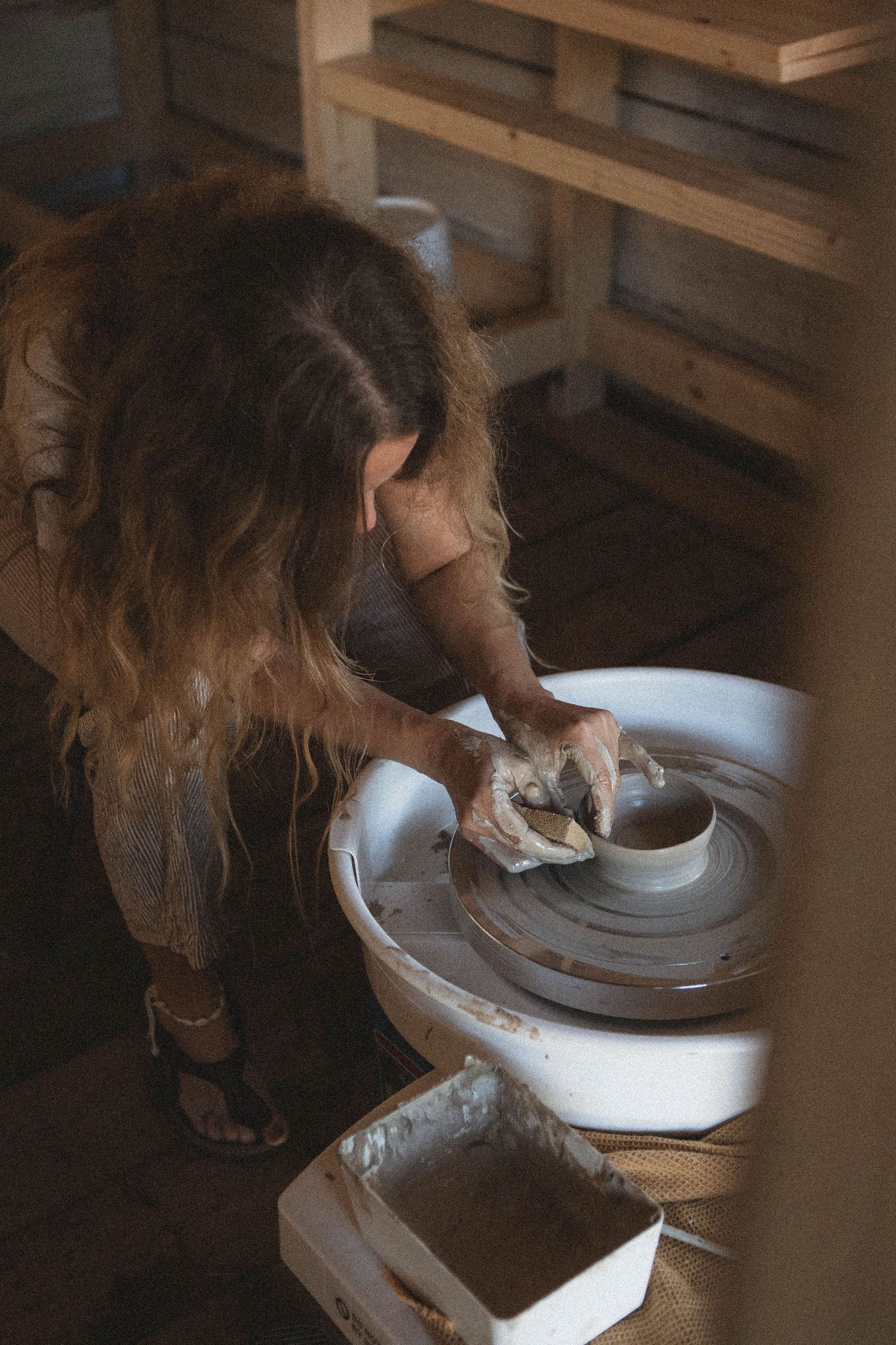Working at a pottery wheel in a rustic studio with wooden shelving.