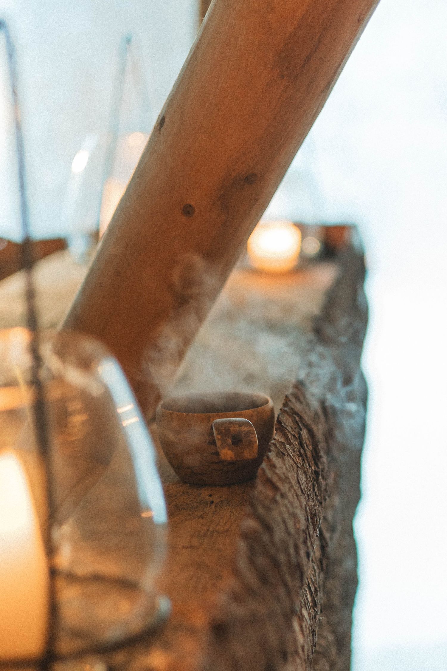 Burning incense stick with smoke trails creates a moody atmosphere next to glowing candles on rustic wood surface.