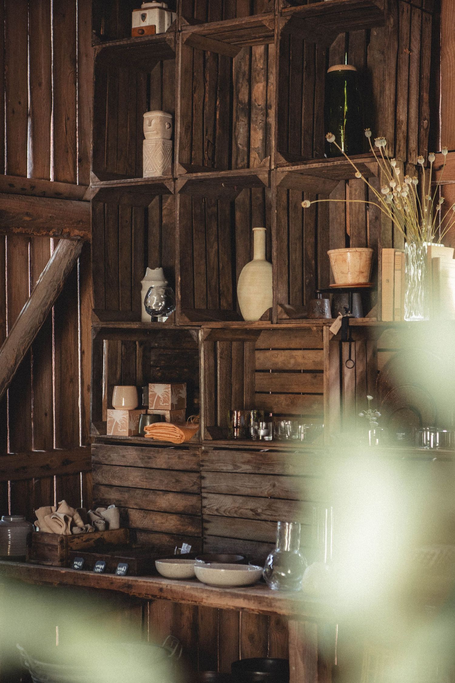 Wooden crate shelving unit with vintage bottles, vases and decor items in rustic setting.