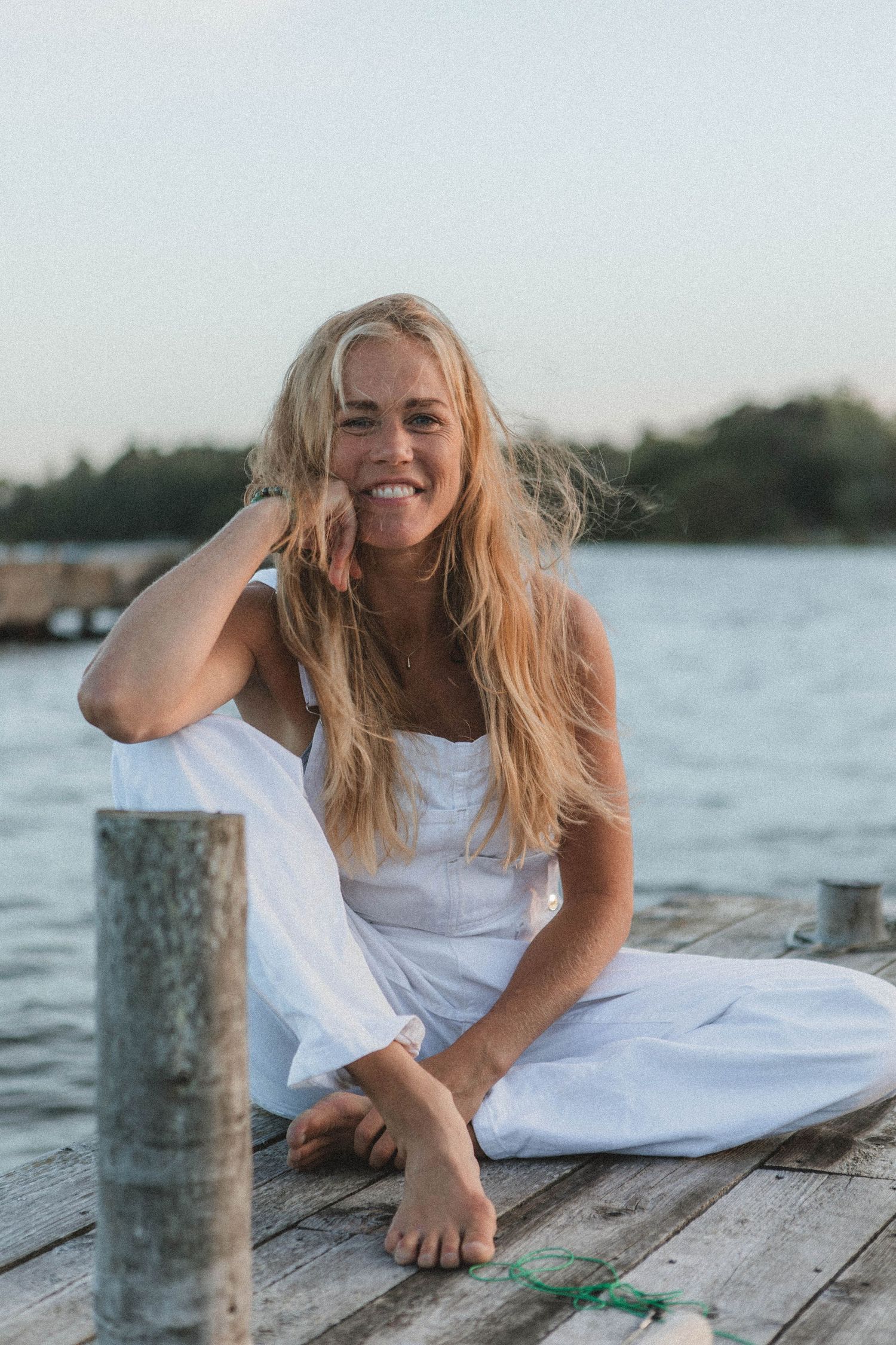 Joyful summer portrait on a wooden dock wearing white clothing by the water.