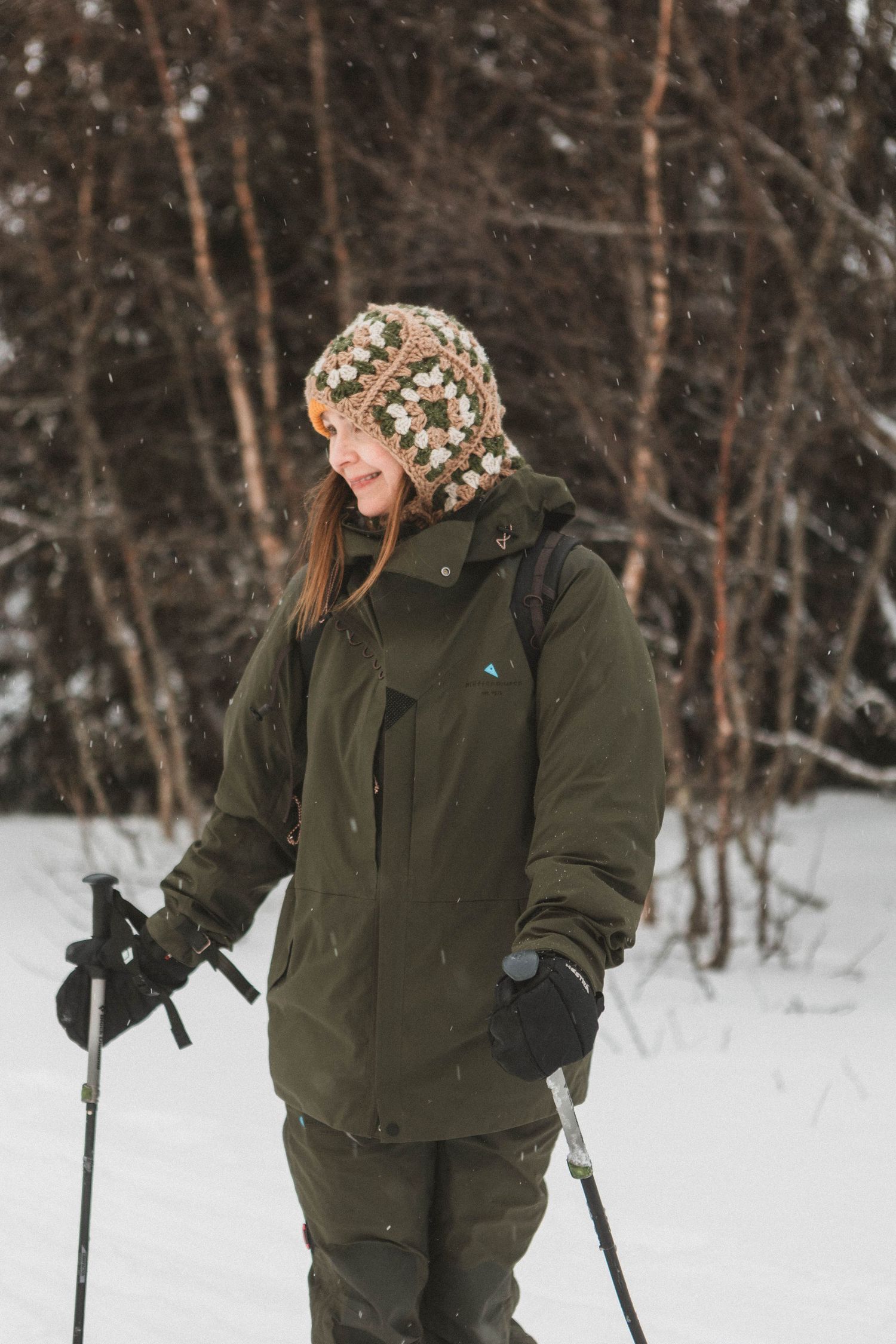 Winter scene showing person in warm winter gear cross-country skiing through snowy forest.