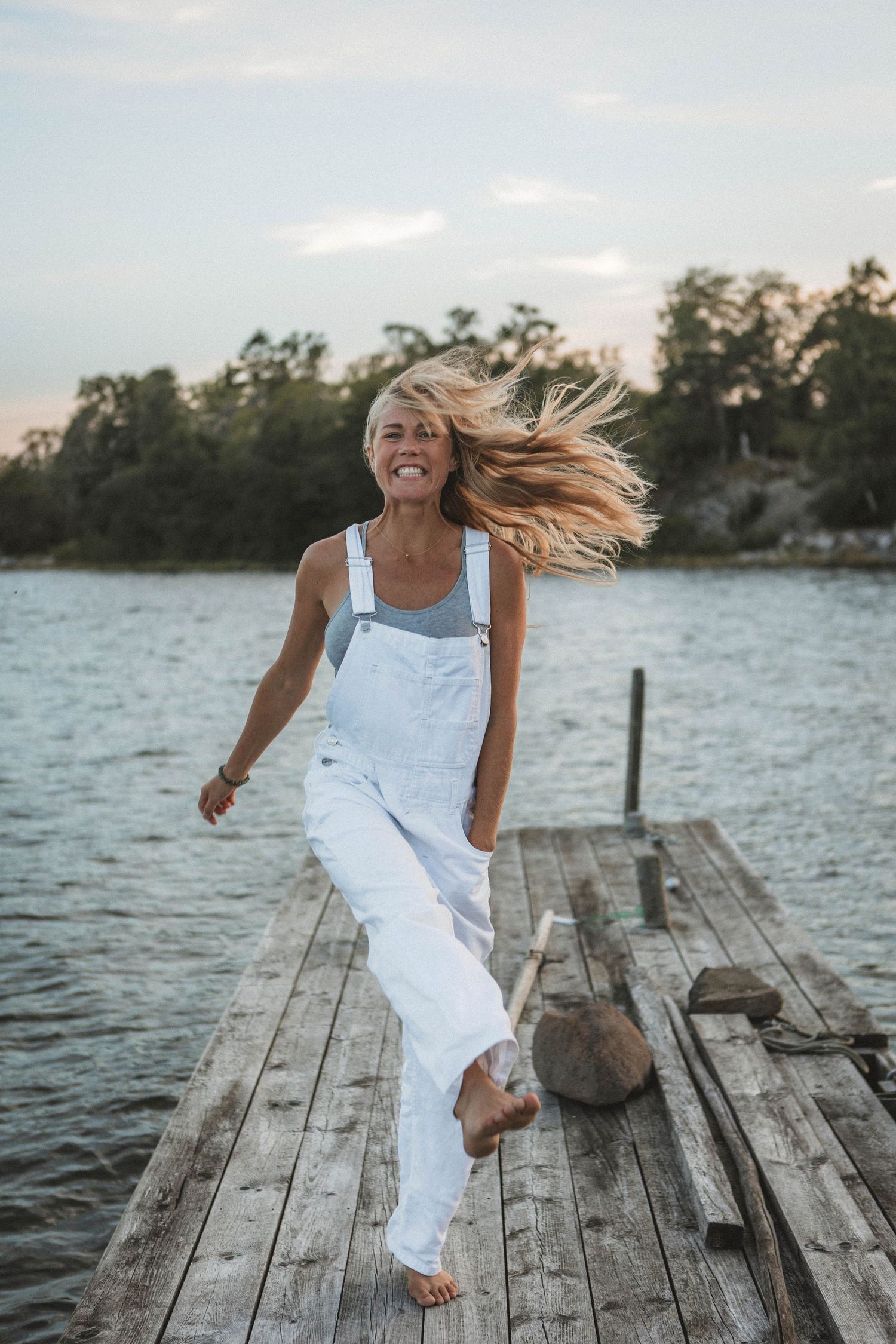 Dynamic shot of someone in white overalls dancing on a wooden pier by the lake.