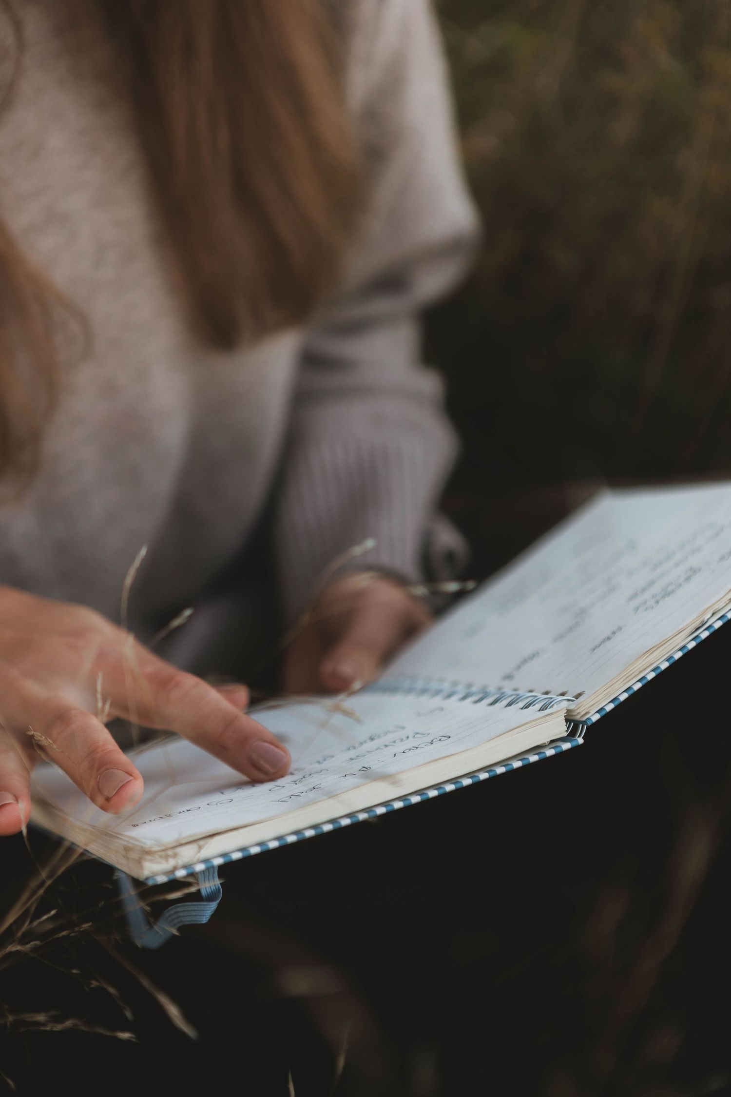 Close-up of hands writing in a spiral notebook against a dark background.