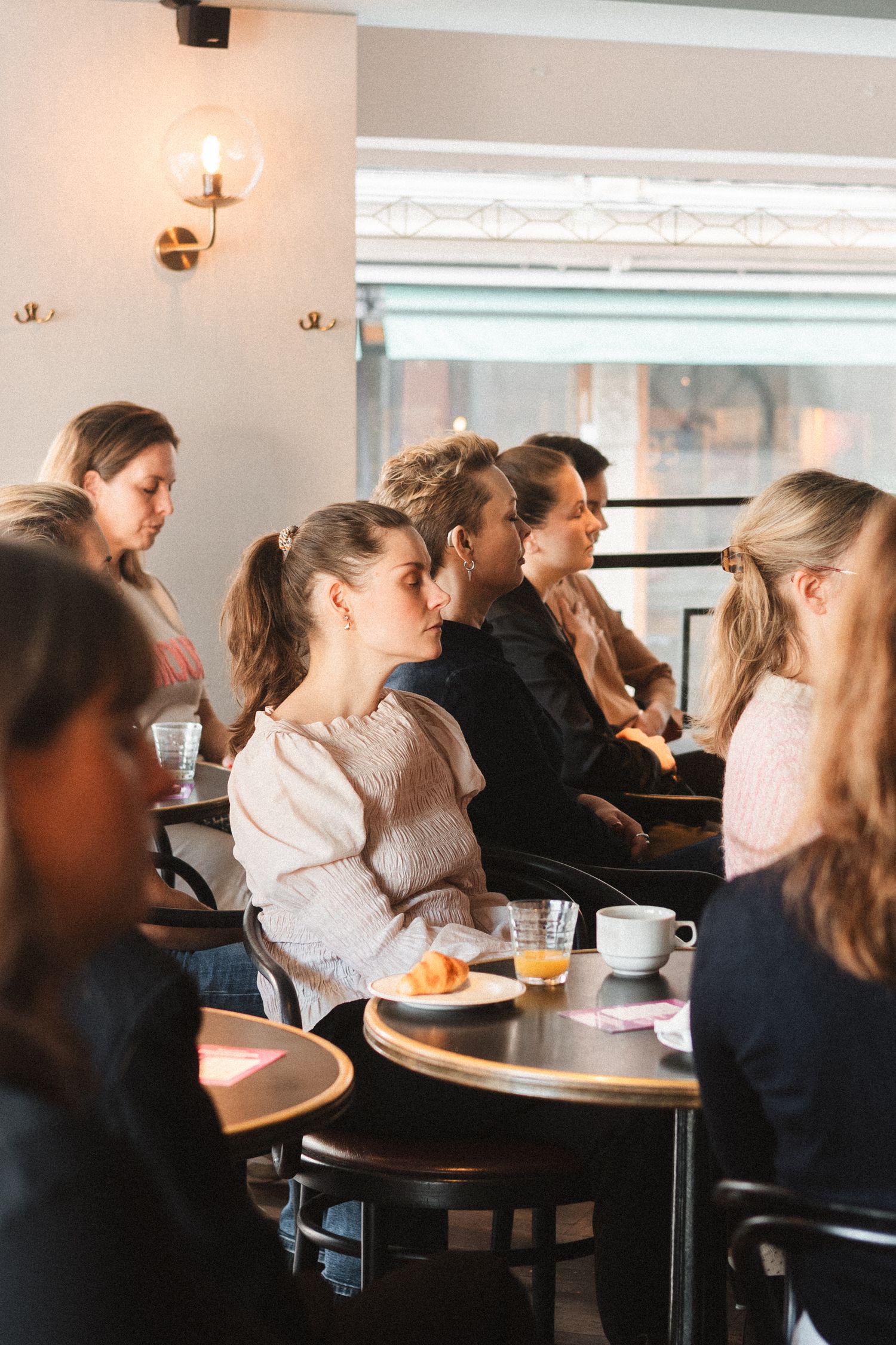 People seated at round tables in a cafe enjoy beverages and snacks during a social gathering.