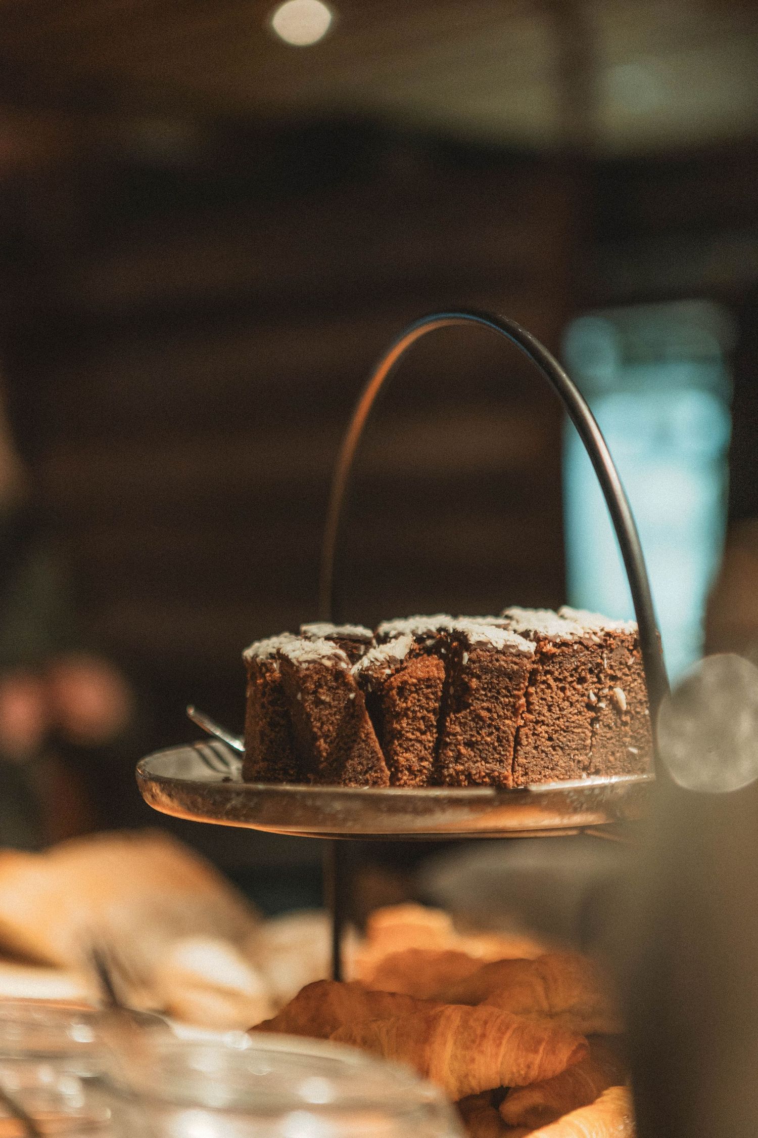 A chocolate cake with powdered sugar displayed on an elegant tiered serving stand in warm lighting.