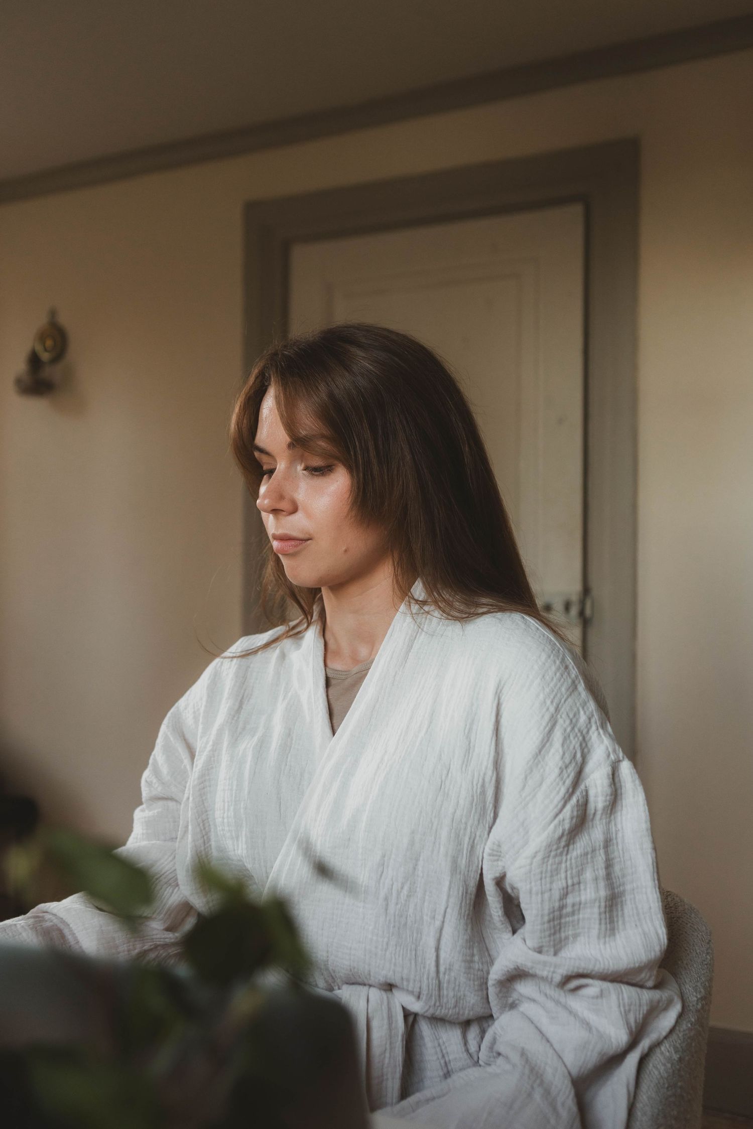 Person in white bathrobe sits thoughtfully in a serene indoor setting with natural lighting.