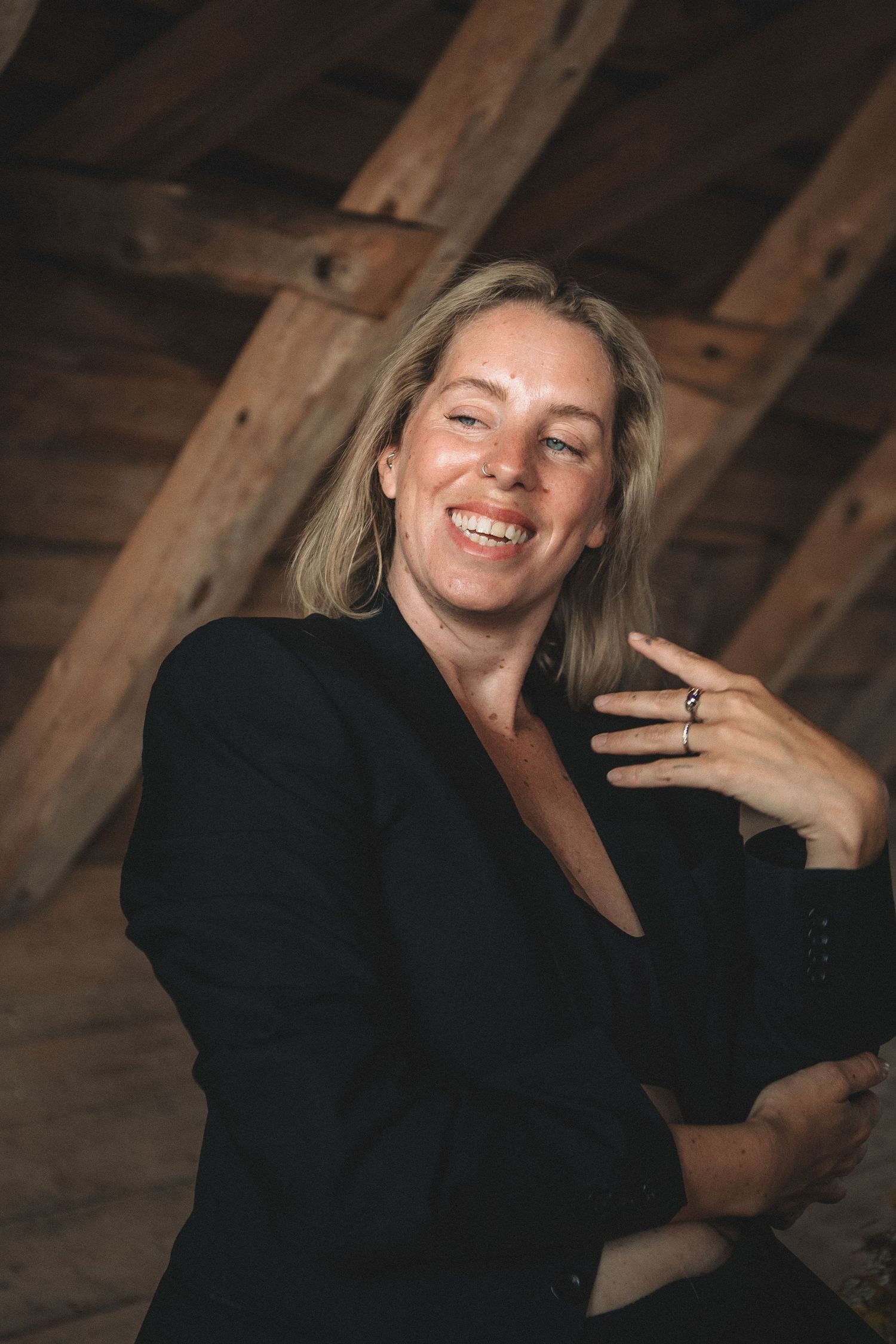 Portrait showing joyful expression in rustic wooden attic setting wearing black blazer.
