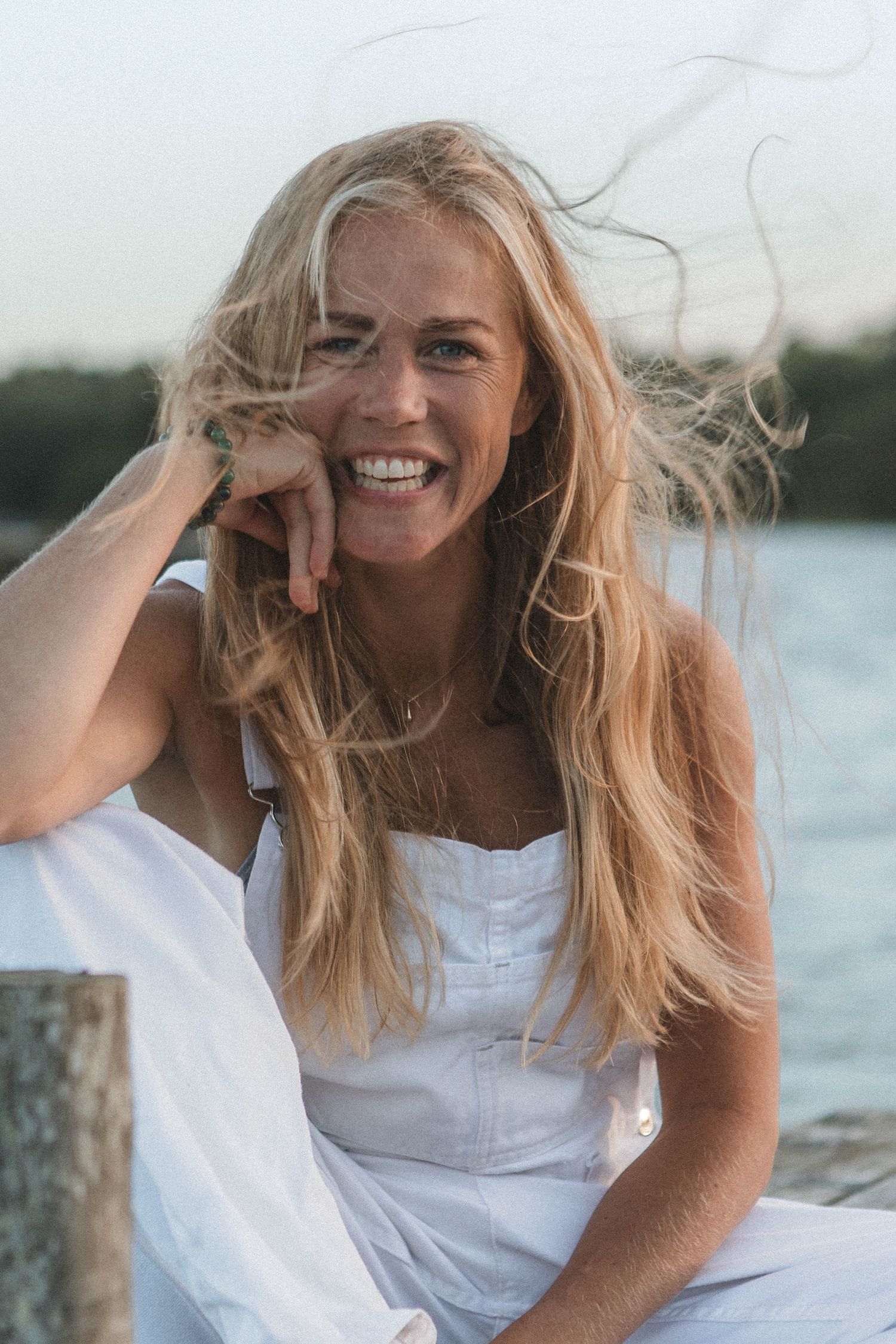 Candid lakeside portrait in a white sundress with windswept hair at sunset.