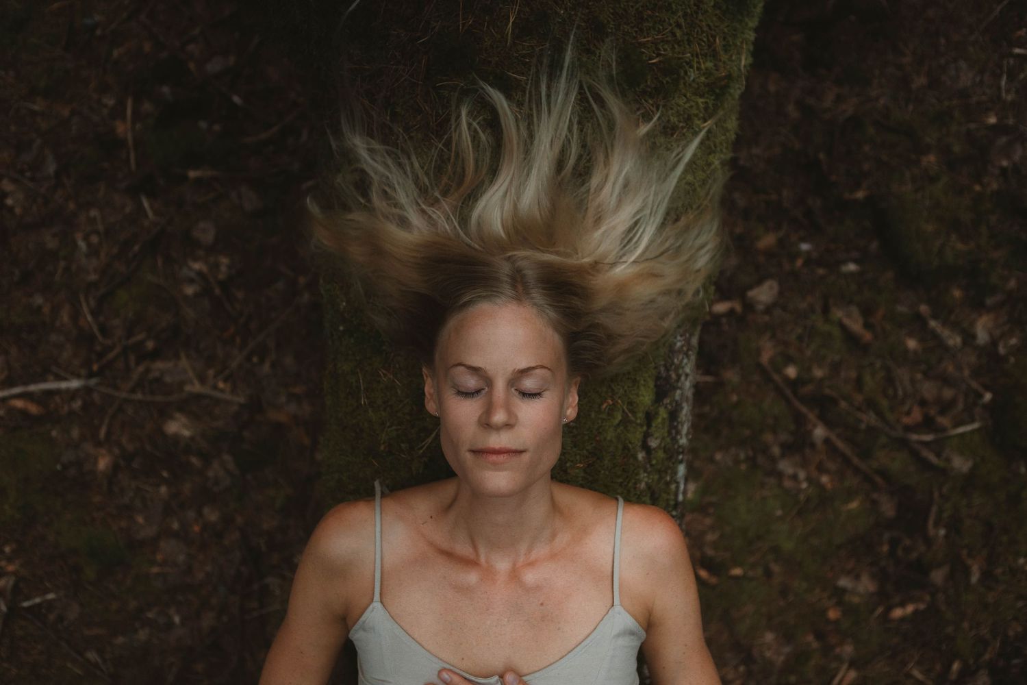 Person lying on forest floor with hair spread out against dark earth.