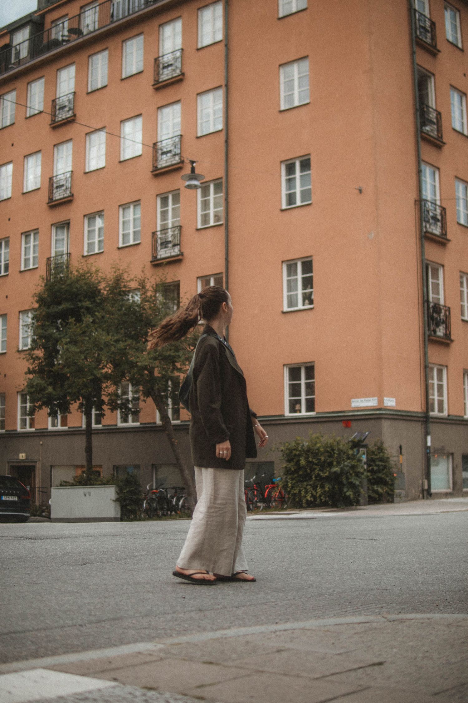 Person in casual attire walking on urban street beside peach-colored apartment building with rows of windows and balconies.