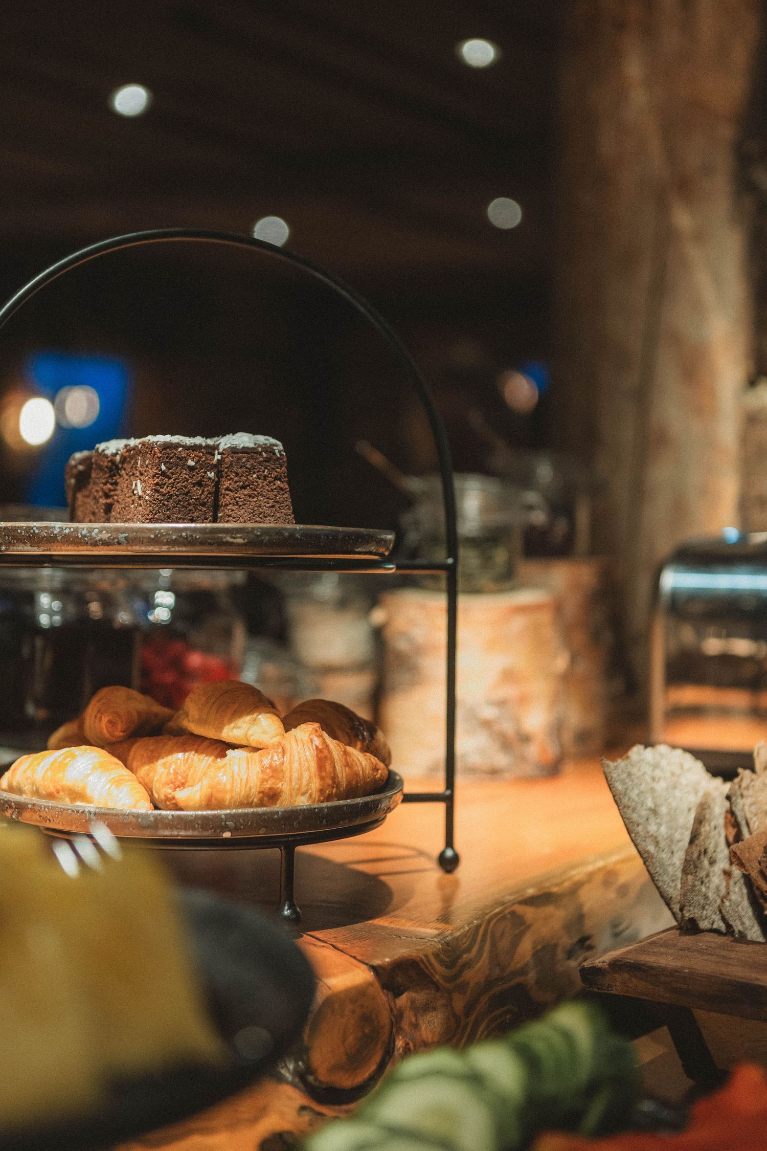 Pastry display stand with croissants and cakes on rustic wooden counter.