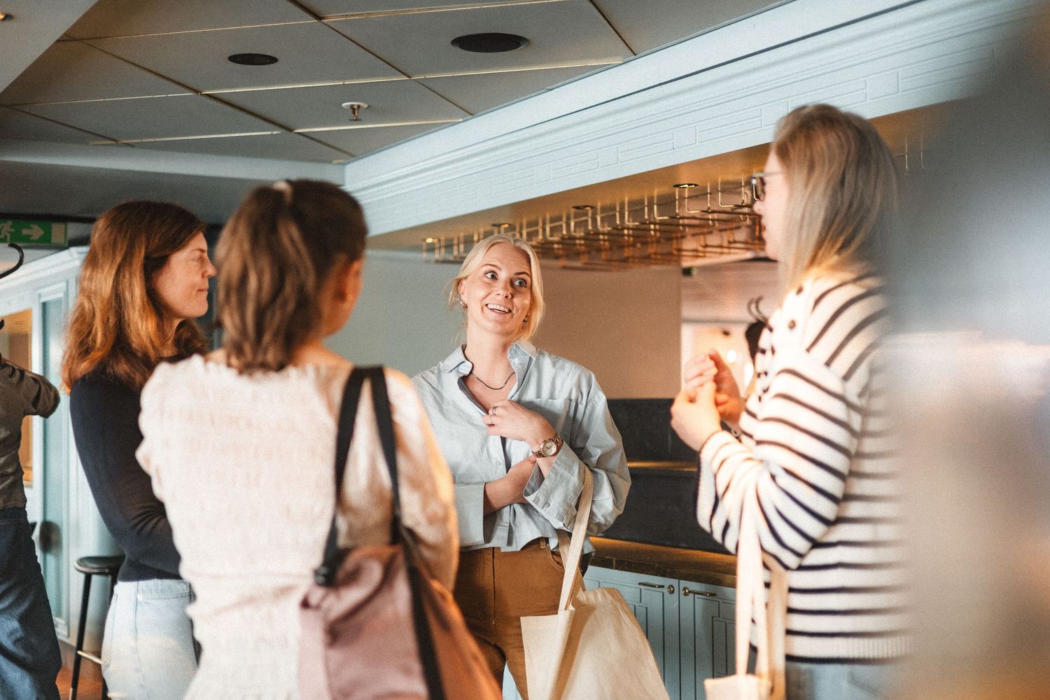 A group of people gather at a bar counter having drinks and engaging in casual conversation.