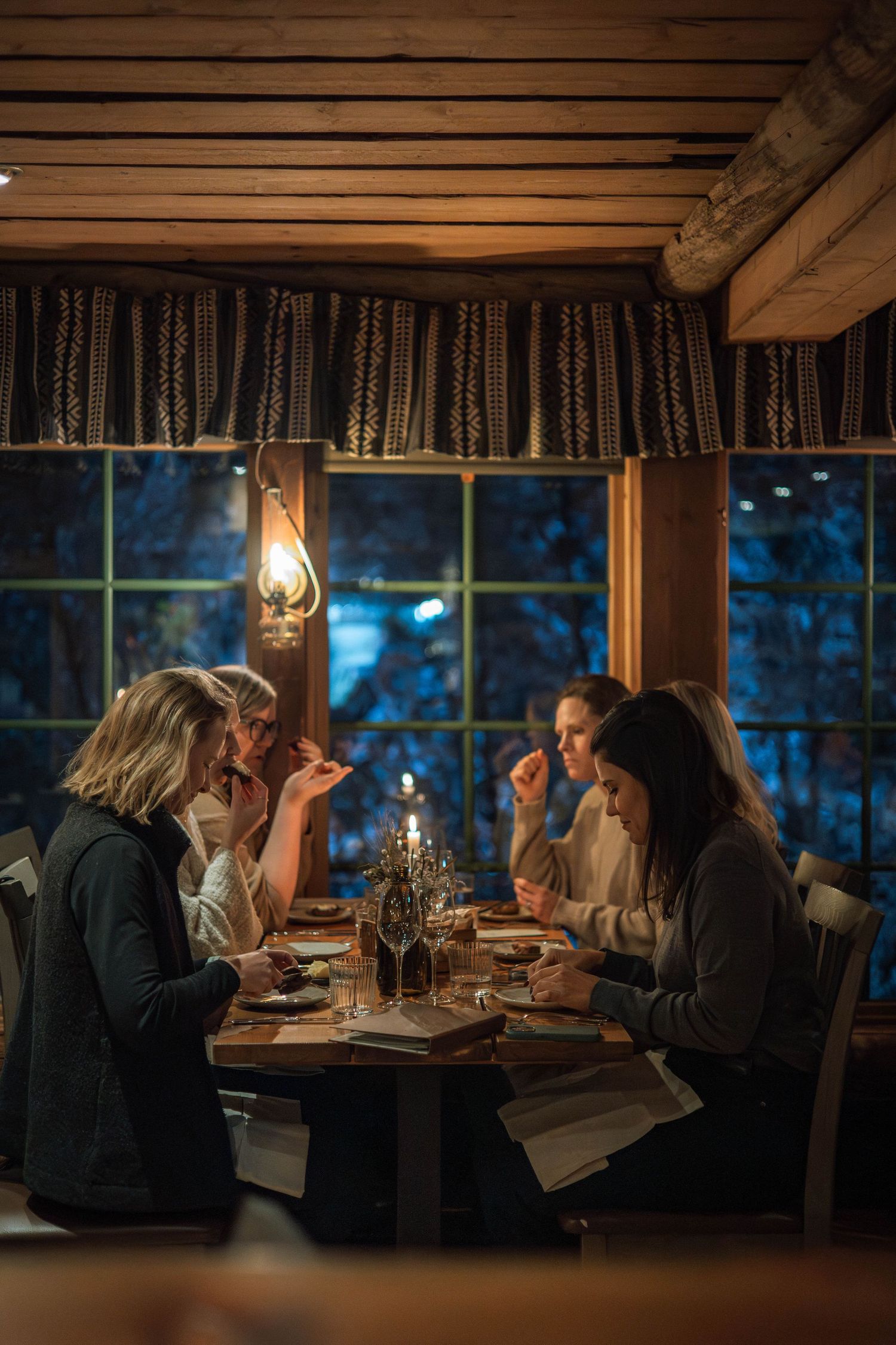 Cozy restaurant interior with oil lamp lighting and diners enjoying dinner at wooden table.