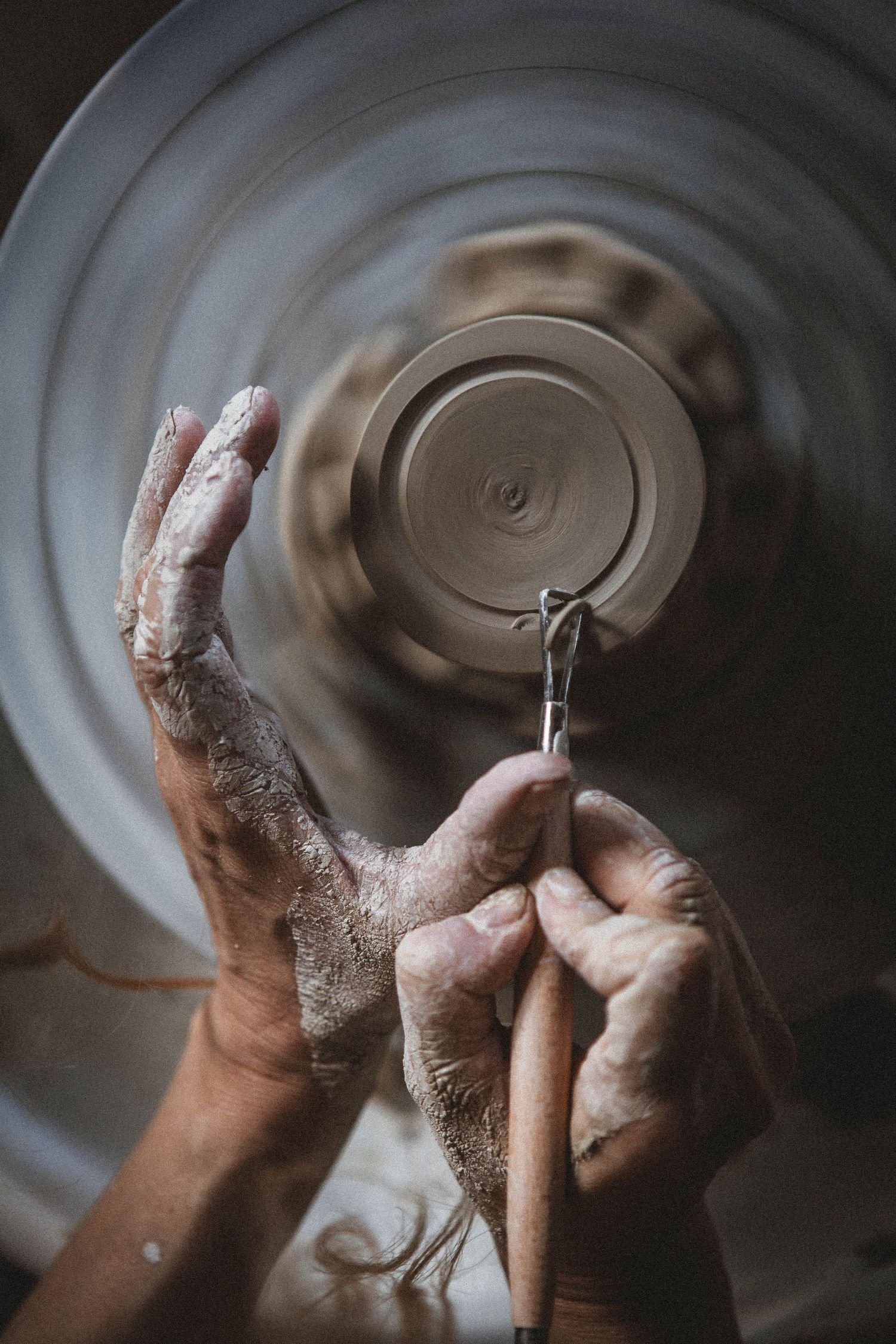 Detailed view of hands sculpting spinning clay on pottery wheel from above.