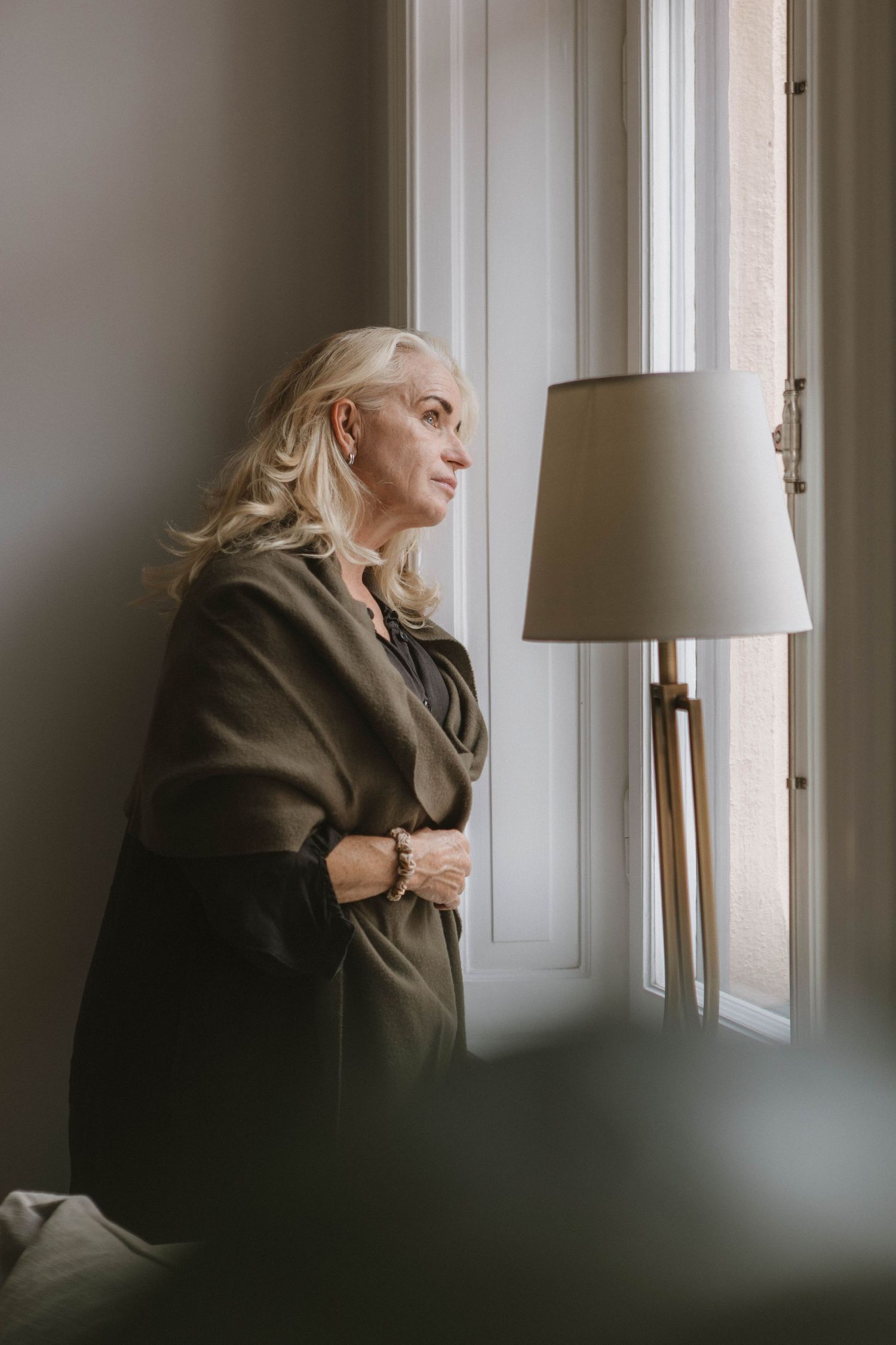 Contemplative pose by window in dark wrap wearing neutral tones.